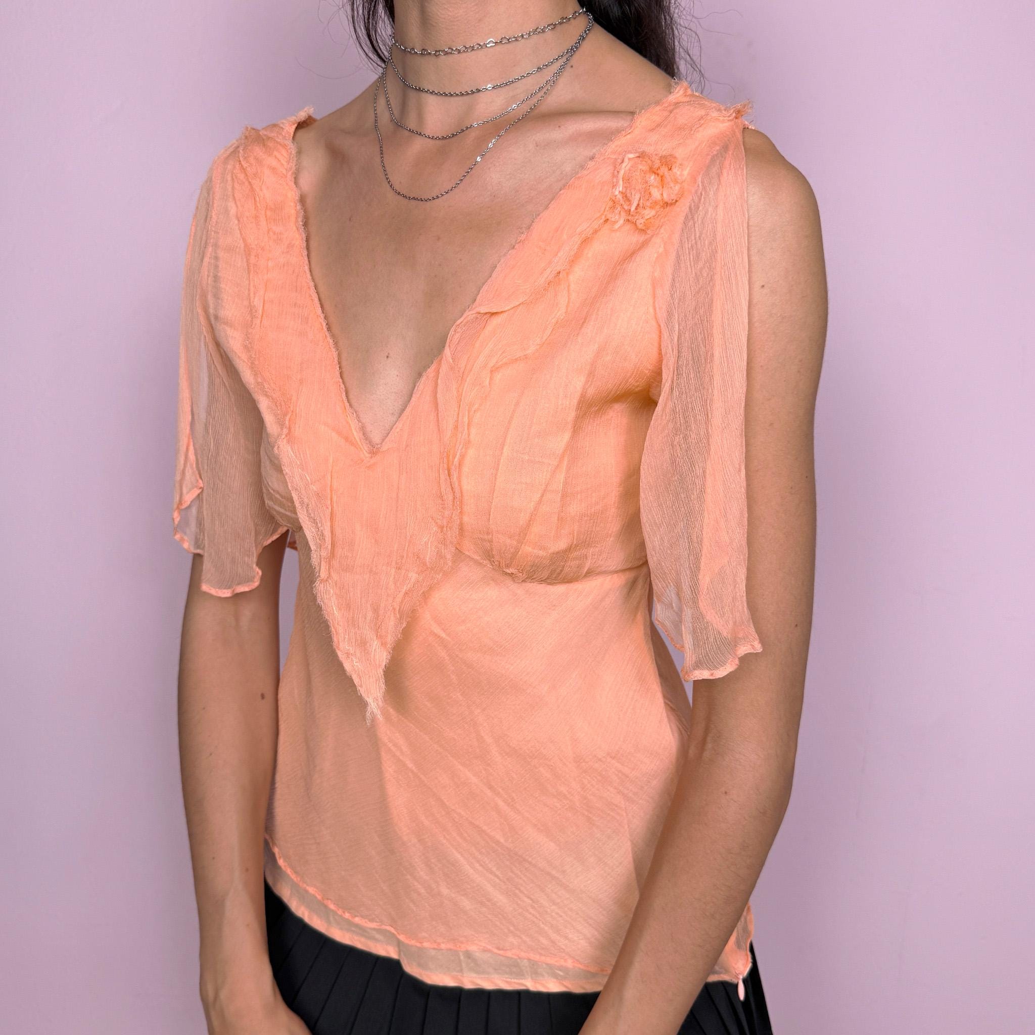 Vintage 2000s pastel light orange-peach fitted top with a deep V-neck, side zip closure, and semi-sheer split flutter sleeves. Romantic, flowy, ethereal design with a soft crinkle texture and a small shoulder rosette, ideal for dreamy summer events or formal looks. Made with a 100% cotton lining and a 100% viscose outer layer. Excellent vintage condition.