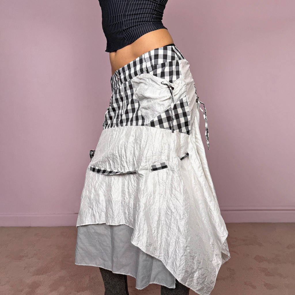 Vintage 2000s white and black midi skirt with deconstructed avant-garde styling, plaid panels, pockets, front zip closure, tie detail, and an asymmetric layered hem with crinkled texture and a striped underlayer. Extravagant artistic statement piece with a rag doll silhouette. Can be worn high waisted for size M or lower rise for sizes XS and S. Made from a polyester and polyamide blend. Great vintage condition.