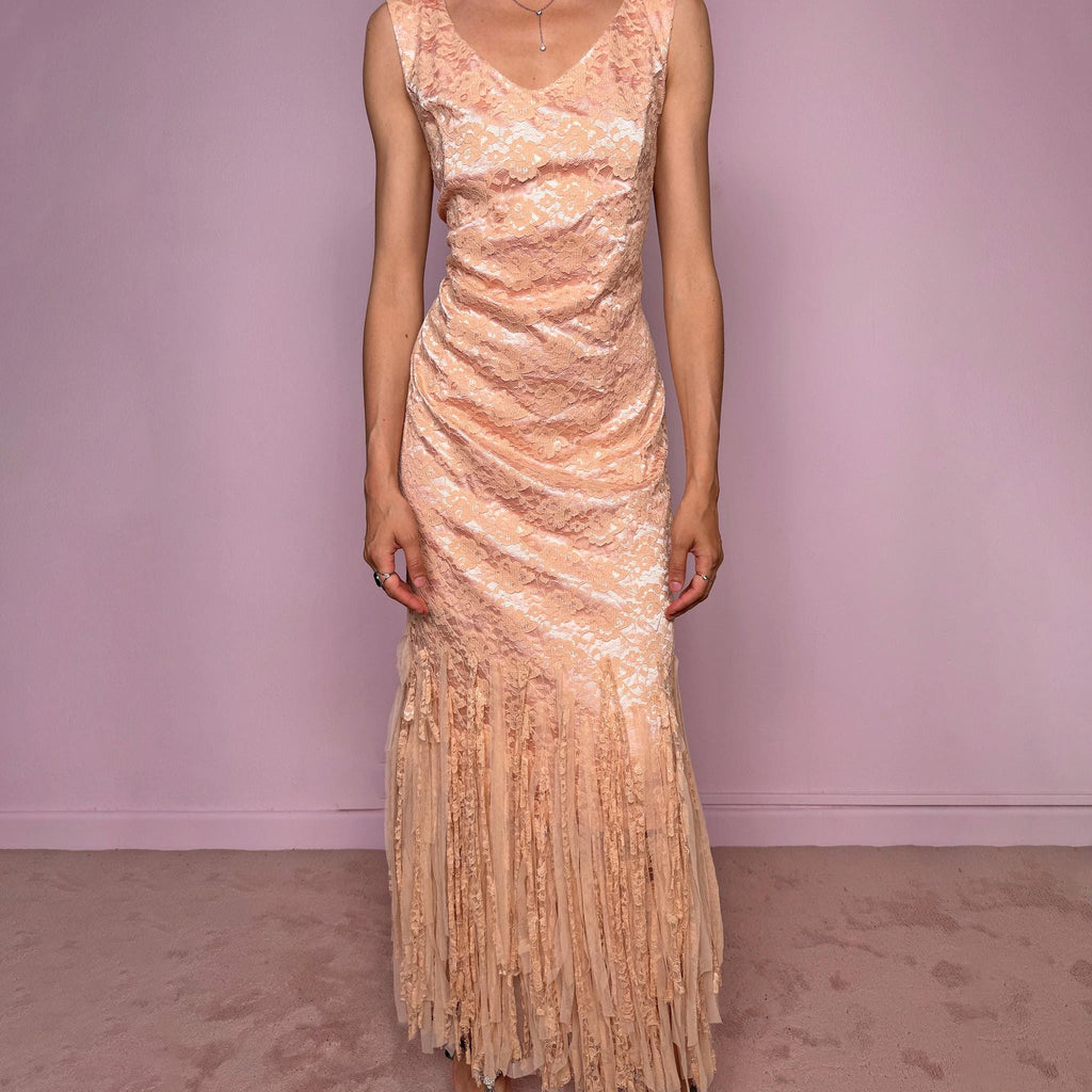 Vintage 2000s pastel peach lace maxi dress. Features a romantic V-neckline, fitted sleeveless silhouette, side zip closure, and a dramatic fringed lace hem. A refined occasion dress in a soft peach, salmon, and blush pink tone, perfect for romantic evening styling, spring-summer events, weddings, or elevated vintage looks. Made in Spain by a Spanish designer, with a nylon-cotton blend outer layer and polyester lining, with no stretch. Excellent vintage condition.