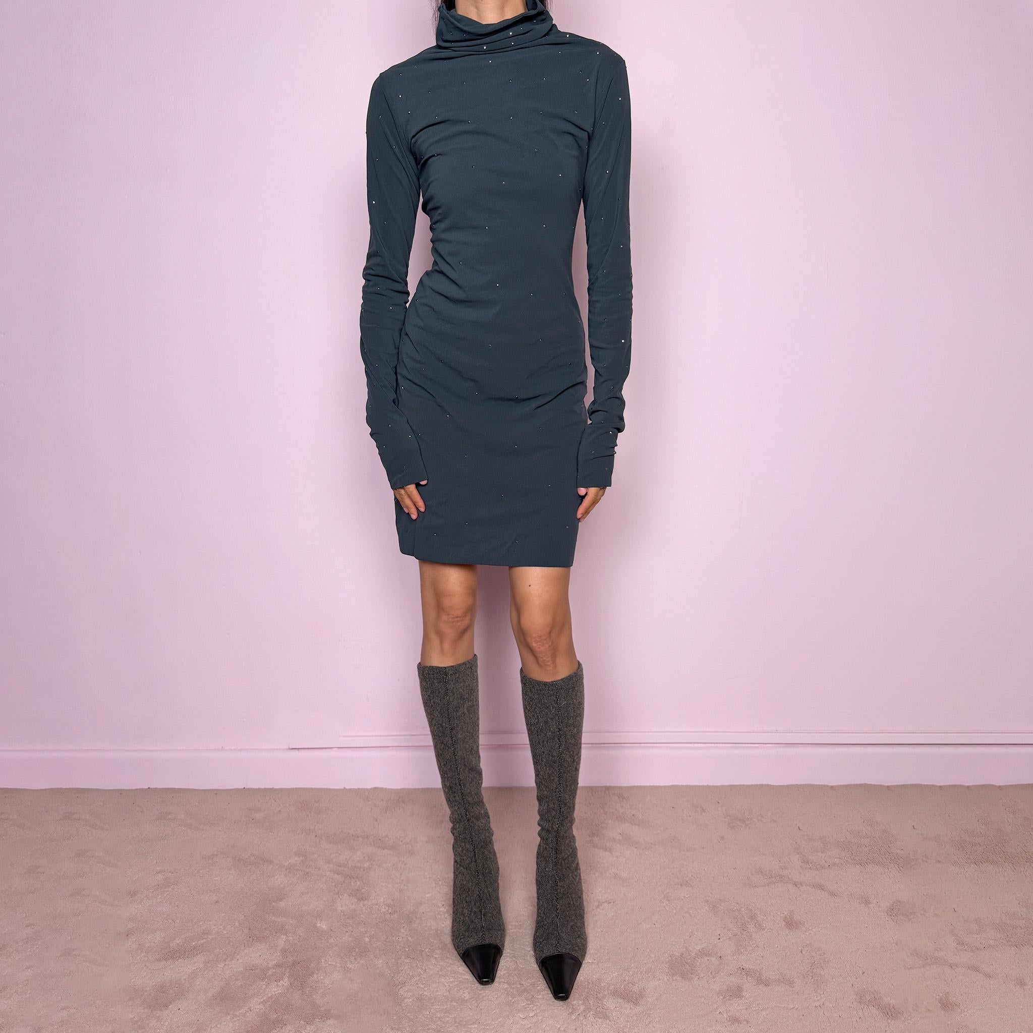 Vintage 2000s gray mini dress made in Italy from a stretchy polyamide-elastane mesh fabric. Features long sleeves, a draped high neckline, a body-skimming silhouette that flares at the hem, and delicate mini studded details throughout. A sleek dark minimal Y2K piece with an avant-garde feel. Excellent vintage condition.