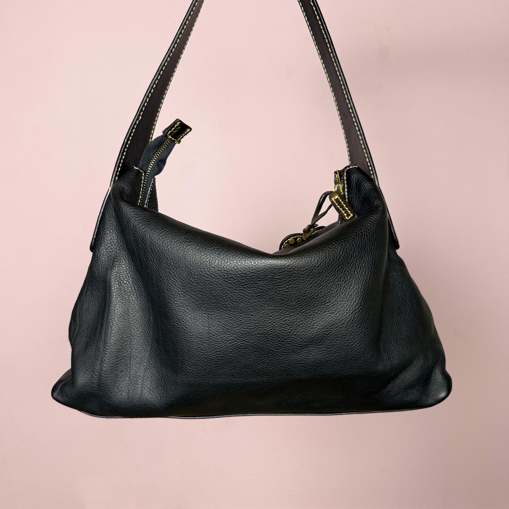 Vintage 2000s black genuine leather shoulder bag made in Italy, Firenze. Features a soft slouchy silhouette, top zip closure, bronze and gold-tone belted front detail, metal eyelets, studded hardware, heart charm, and decorative padlock accent. A unique Y2K Italian leather statement bag with a biker-boho glam and indie grunge feel.