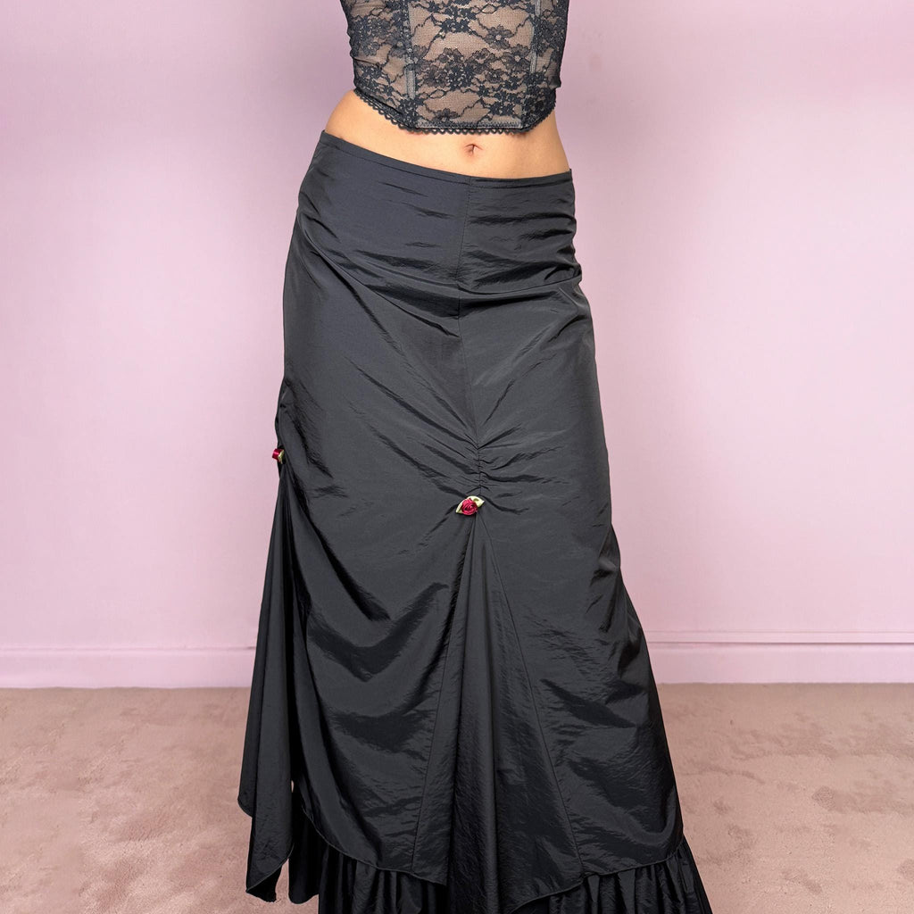 Vintage 2000s black layered ruched midi skirt with a dark gothic avant-garde feel. Back zip closure, structured non-stretch fabric, gathered front ruching, asymmetric layered paneling, ruffled hem, and small floral details. Can be worn high waisted for M or lower rise for S and XS. Made from 100% polyamide with lining 100% polyester. Excellent vintage condition.