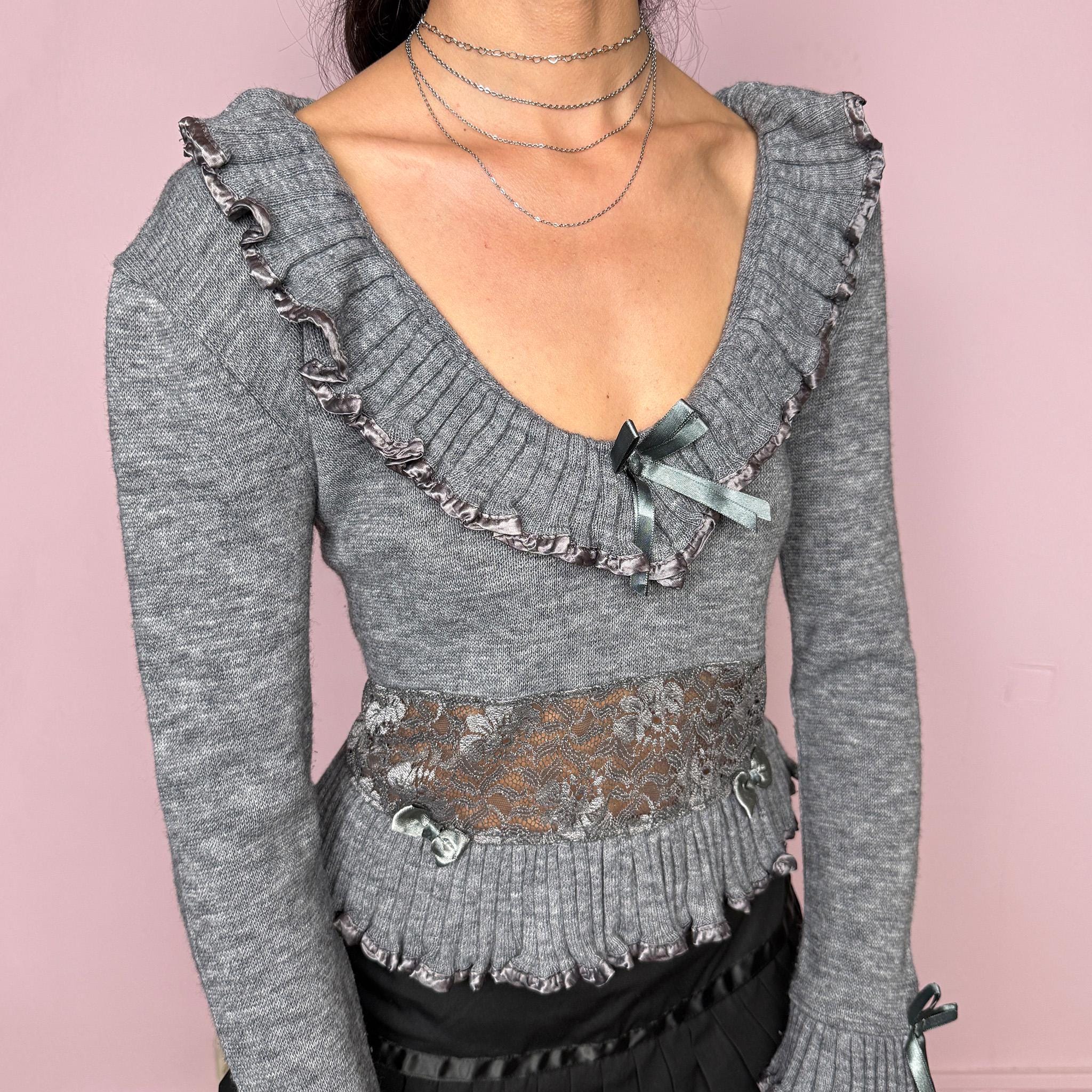 Vintage 2000s gray knit sweater featuring a lace waist panel, delicate ruffle trims, satin bow details, and romantic flared cuffs. Designed with a soft feminine silhouette, deep scoop neckline, and a dreamy coquette and balletcore feel. Made from 70% acrylic and 30% wool. Great vintage condition.