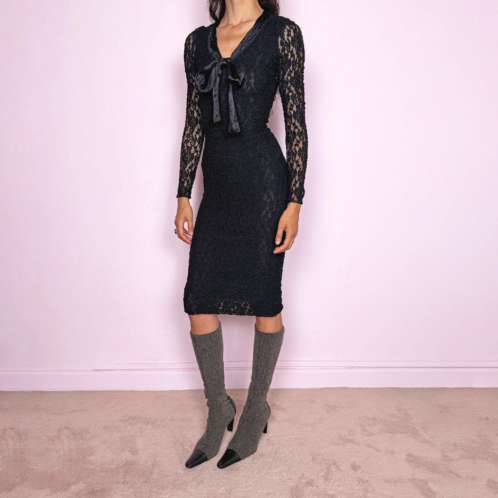 Vintage 2000s D&G Dolce & Gabbana black long sleeve midi dress crafted from stretchy silk-blend textured lace fabric. Fitted silhouette with sheer long sleeves, side zip closure, and satin bow tie detail at the neckline. A dark romantic designer piece with a sharp feminine silhouette, perfect for evening wear. Main fabric is polyamide and silk blend; lining is 93% silk and 7% elastane. Excellent vintage condition.