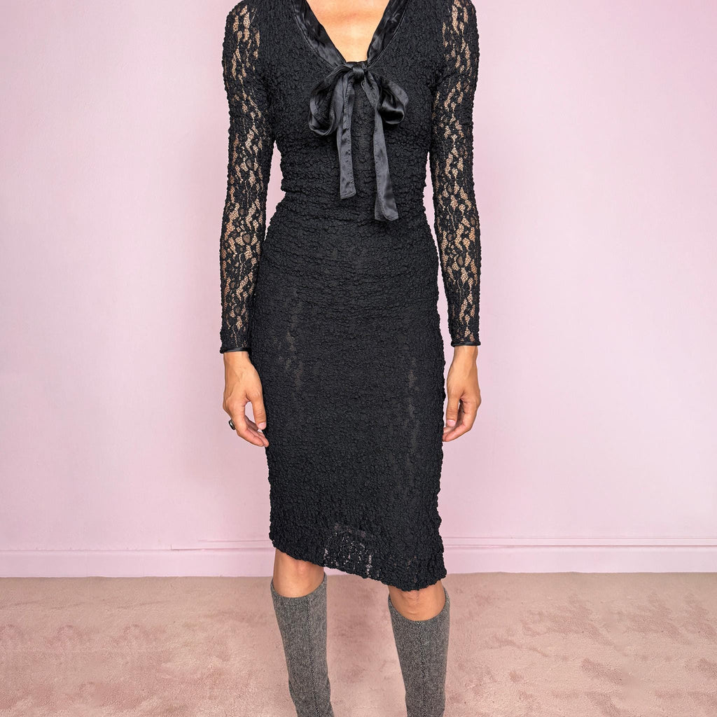 Vintage 2000s D&G Dolce & Gabbana black long sleeve midi dress crafted from stretchy silk-blend textured lace fabric. Fitted silhouette with sheer long sleeves, side zip closure, and satin bow tie detail at the neckline. A dark romantic designer piece with a sharp feminine silhouette, perfect for evening wear. Main fabric is polyamide and silk blend; lining is 93% silk and 7% elastane. Excellent vintage condition.