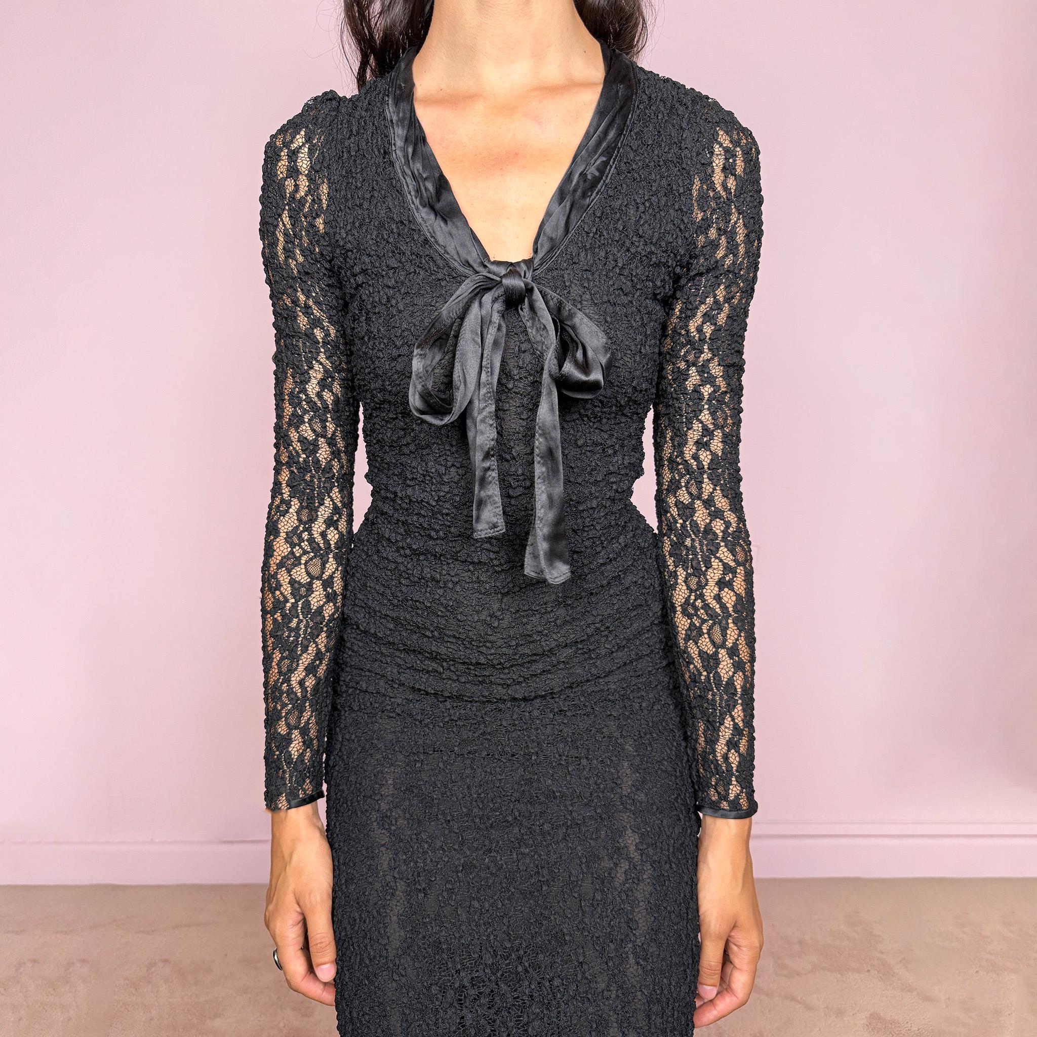 Vintage 2000s D&G Dolce & Gabbana black long sleeve midi dress crafted from stretchy silk-blend textured lace fabric. Fitted silhouette with sheer long sleeves, side zip closure, and satin bow tie detail at the neckline. A dark romantic designer piece with a sharp feminine silhouette, perfect for evening wear. Main fabric is polyamide and silk blend; lining is 93% silk and 7% elastane. Excellent vintage condition.
