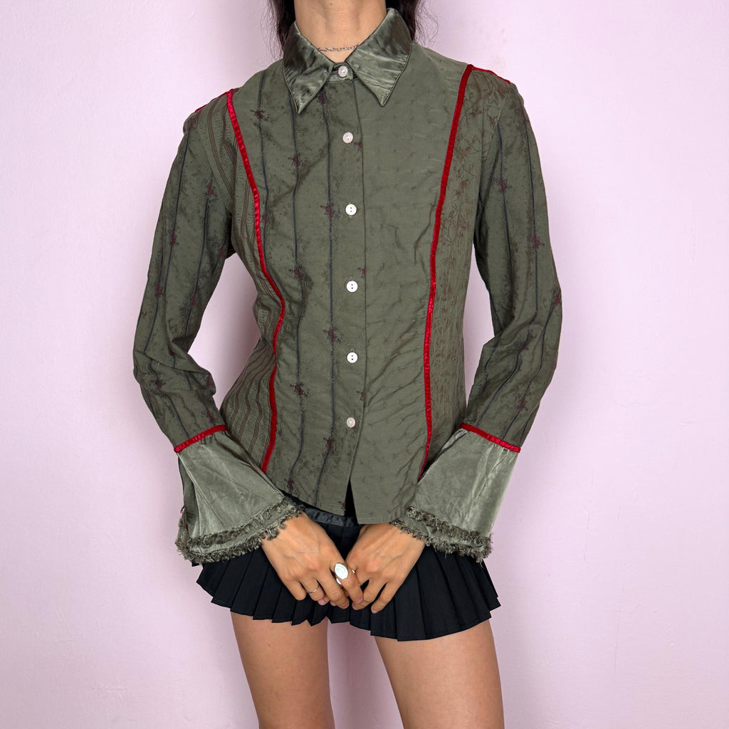Vintage 2000s muted olive green blouse with subtle floral texture, button-front closure, sharp pointed collar, vertical paneling, contrasting red velvet trim, satin-like collar and cuff details, flared sleeves, and softly frayed edges for elevated earthy styling. Composition label is missing, so the exact fabric is unknown. Great vintage condition.