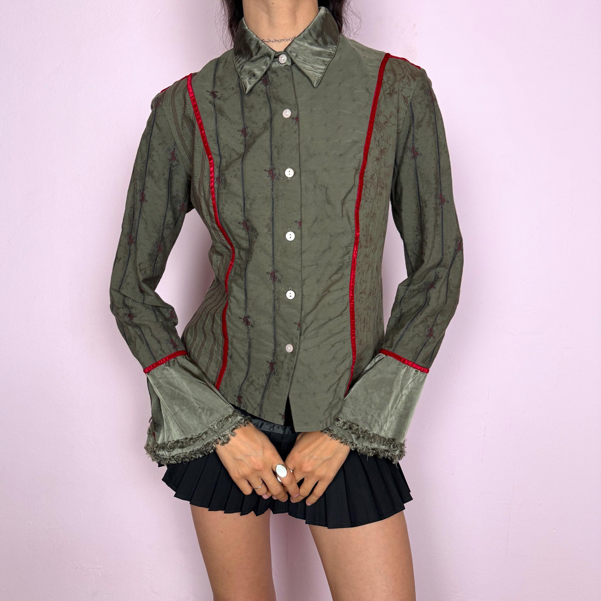 Vintage 2000s muted olive green blouse with subtle floral texture, button-front closure, sharp pointed collar, vertical paneling, contrasting red velvet trim, satin-like collar and cuff details, flared sleeves, and softly frayed edges for elevated earthy styling. Composition label is missing, so the exact fabric is unknown. Great vintage condition.