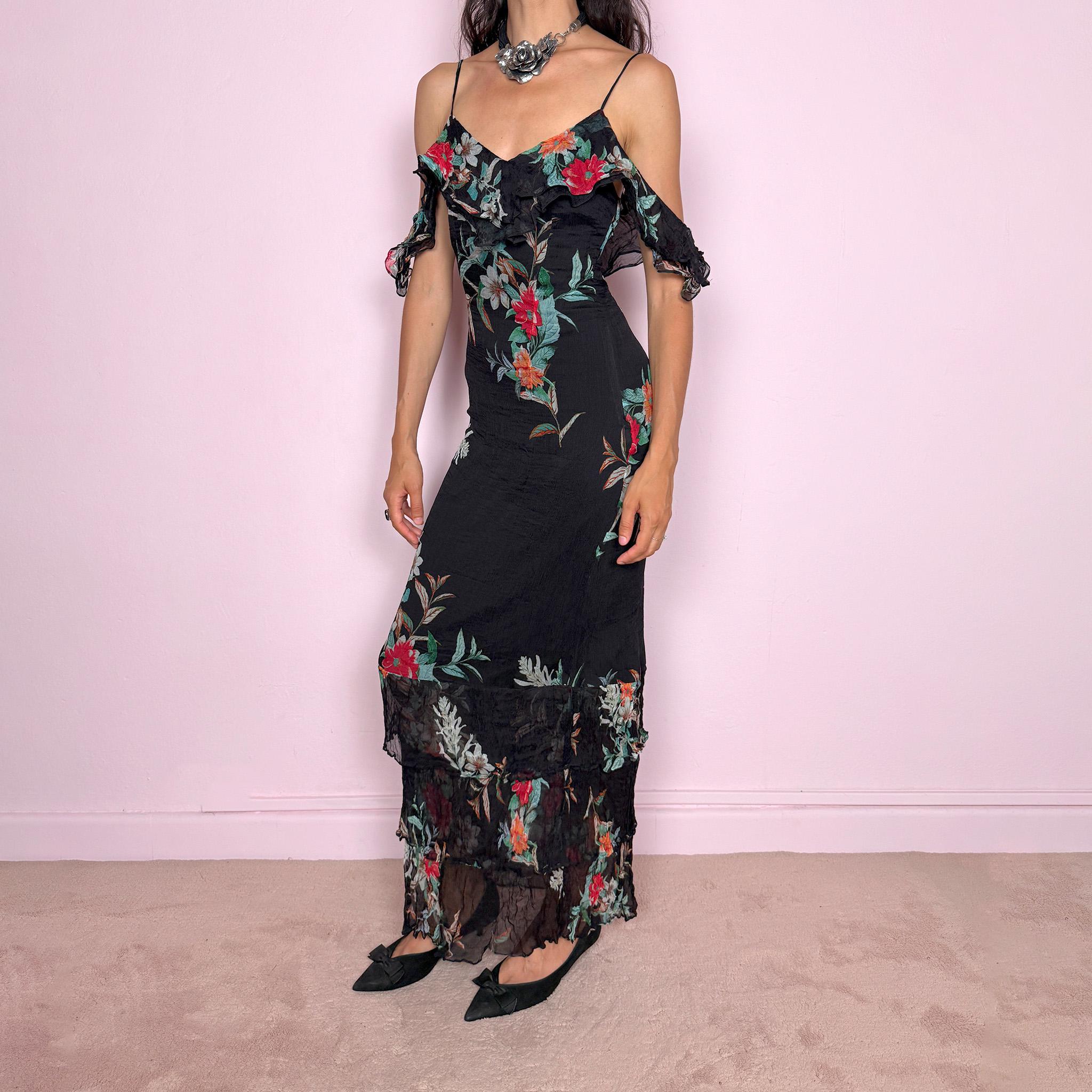 Vintage 2000s Guess Los Angeles black floral maxi dress with a romantic off-shoulder silhouette, delicate adjustable spaghetti straps, and dramatic ruffle detailing across the bust and sleeves. Designed with a fitted body, side zip closure, softly flared maxi skirt, and sheer textured floral panels through the hem. A dreamy statement evening dress, perfect for summer occasions.