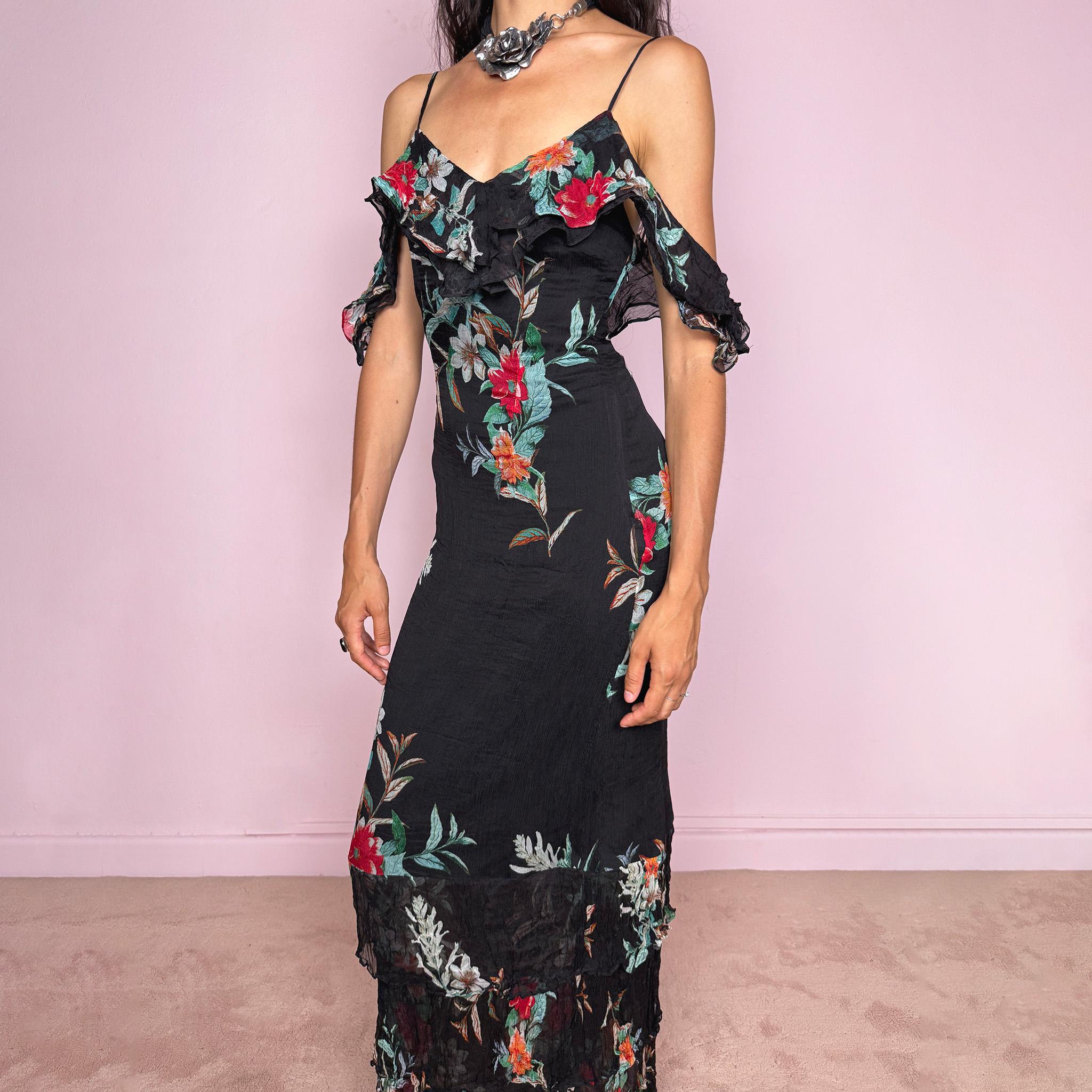 Vintage 2000s Guess Los Angeles black floral maxi dress with a romantic off-shoulder silhouette, delicate adjustable spaghetti straps, and dramatic ruffle detailing across the bust and sleeves. Designed with a fitted body, side zip closure, softly flared maxi skirt, and sheer textured floral panels through the hem. A dreamy statement evening dress, perfect for summer occasions.