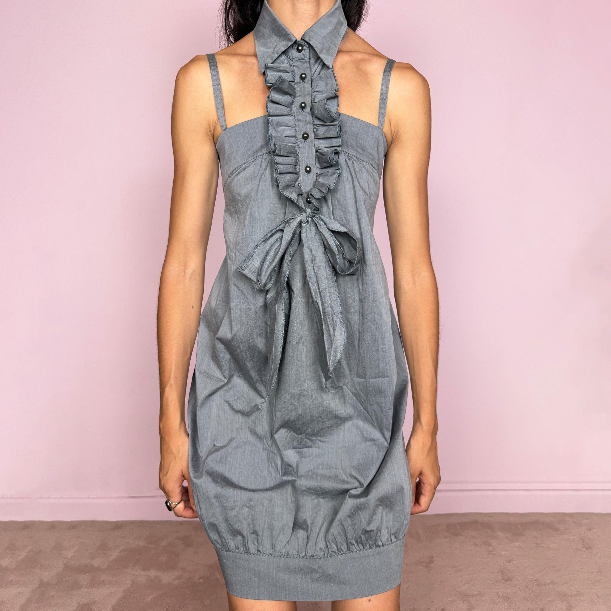 Vintage 2000s Cop Copine gray mini dress designed in a structured fabric with no stretch, featuring adjustable straps, a distinctive attached shirt-style collar with a ruffled button-front panel, a gathered bust, a tie-front bow, and a relaxed mini silhouette finished with a subtle bubble hem for a sculptural shape. A playful French design Y2K piece with an avant-garde feel, balancing tailoring and romantic doll-like styling with an office-inspired edge.