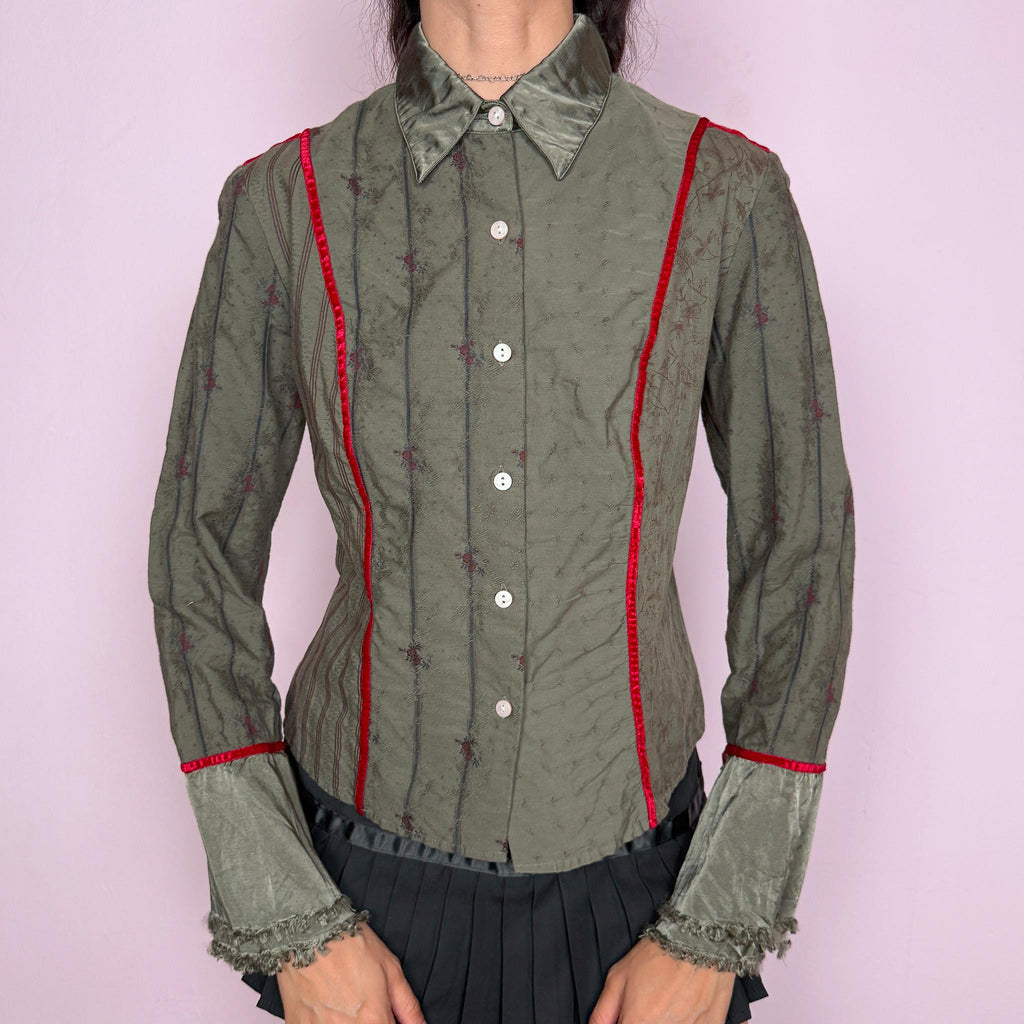 Vintage 2000s muted olive green blouse with subtle floral texture, button-front closure, sharp pointed collar, vertical paneling, contrasting red velvet trim, satin-like collar and cuff details, flared sleeves, and softly frayed edges for elevated earthy styling. Composition label is missing, so the exact fabric is unknown. Great vintage condition.