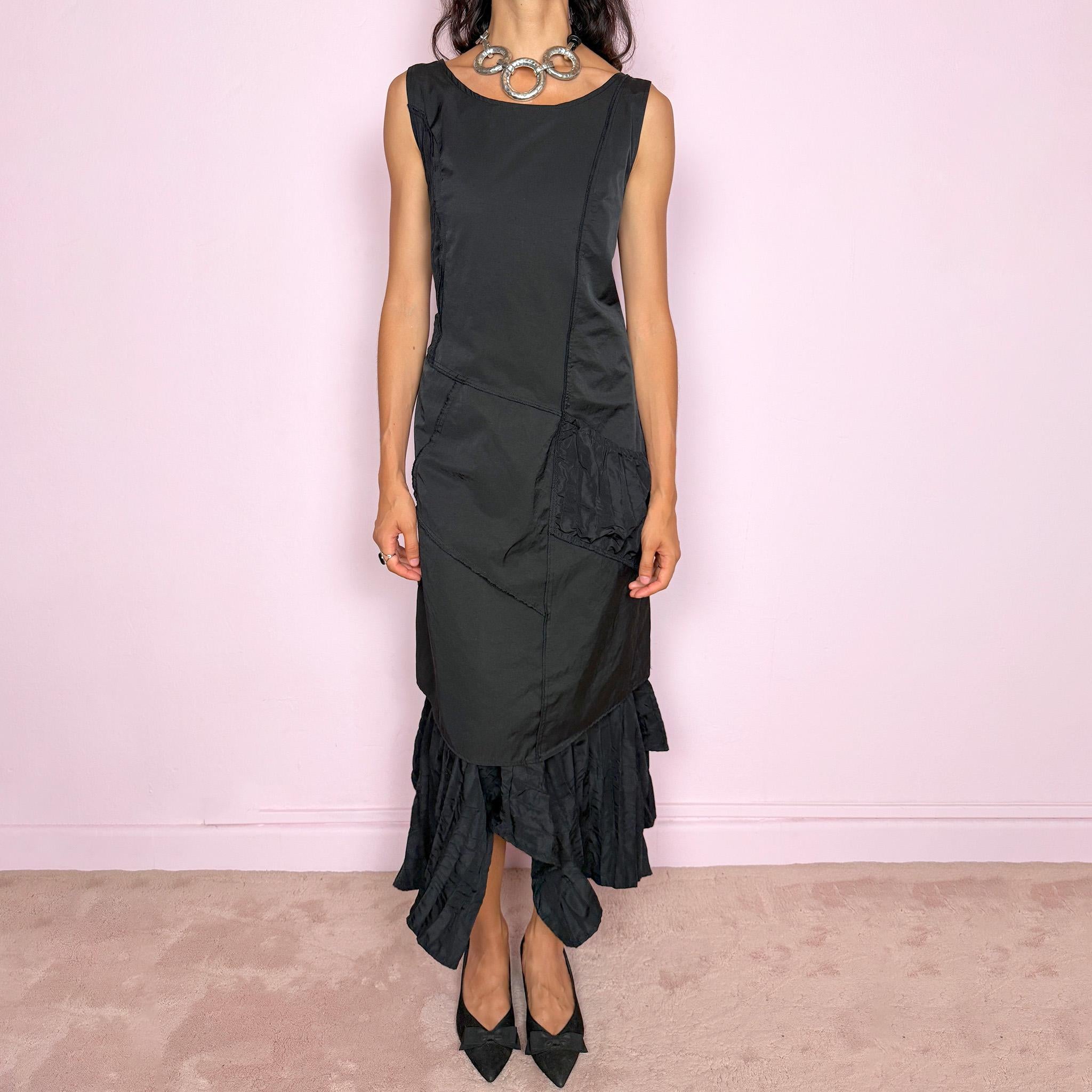 Vintage 2000s black midi dress designed in a structured no-stretch fabric with a side zip closure and an asymmetric panelled silhouette. It features a sleeveless scoop neckline, fitted upper body, diagonal seam construction, and an irregular ruffled hem with crinkled texture for sculptural movement. A dark romantic piece with an understated avant-garde feel, perfect for a minimal gothic look. Made by a French brand from 55% polyamide and 45% cotton, with a 100% polyester lining.