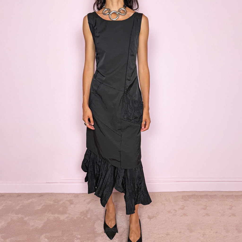 Vintage 2000s black midi dress designed in a structured no-stretch fabric with a side zip closure and an asymmetric panelled silhouette. It features a sleeveless scoop neckline, fitted upper body, diagonal seam construction, and an irregular ruffled hem with crinkled texture for sculptural movement. A dark romantic piece with an understated avant-garde feel, perfect for a minimal gothic look. Made by a French brand from 55% polyamide and 45% cotton, with a 100% polyester lining.