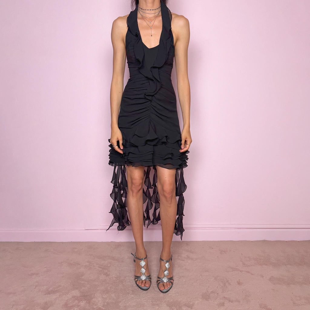 Vintage 90s black halter dress with a dramatic evening silhouette, deep V neckline, fitted bodice, ruched front detailing, layered ruffle trim, and sheer asymmetric hem with trailing chiffon-style back panels. Features a back zip closure and structured body-skimming fit with no stretch. Ideal for extravagant dancey soirées. Made from 100% polyester. Excellent vintage condition.