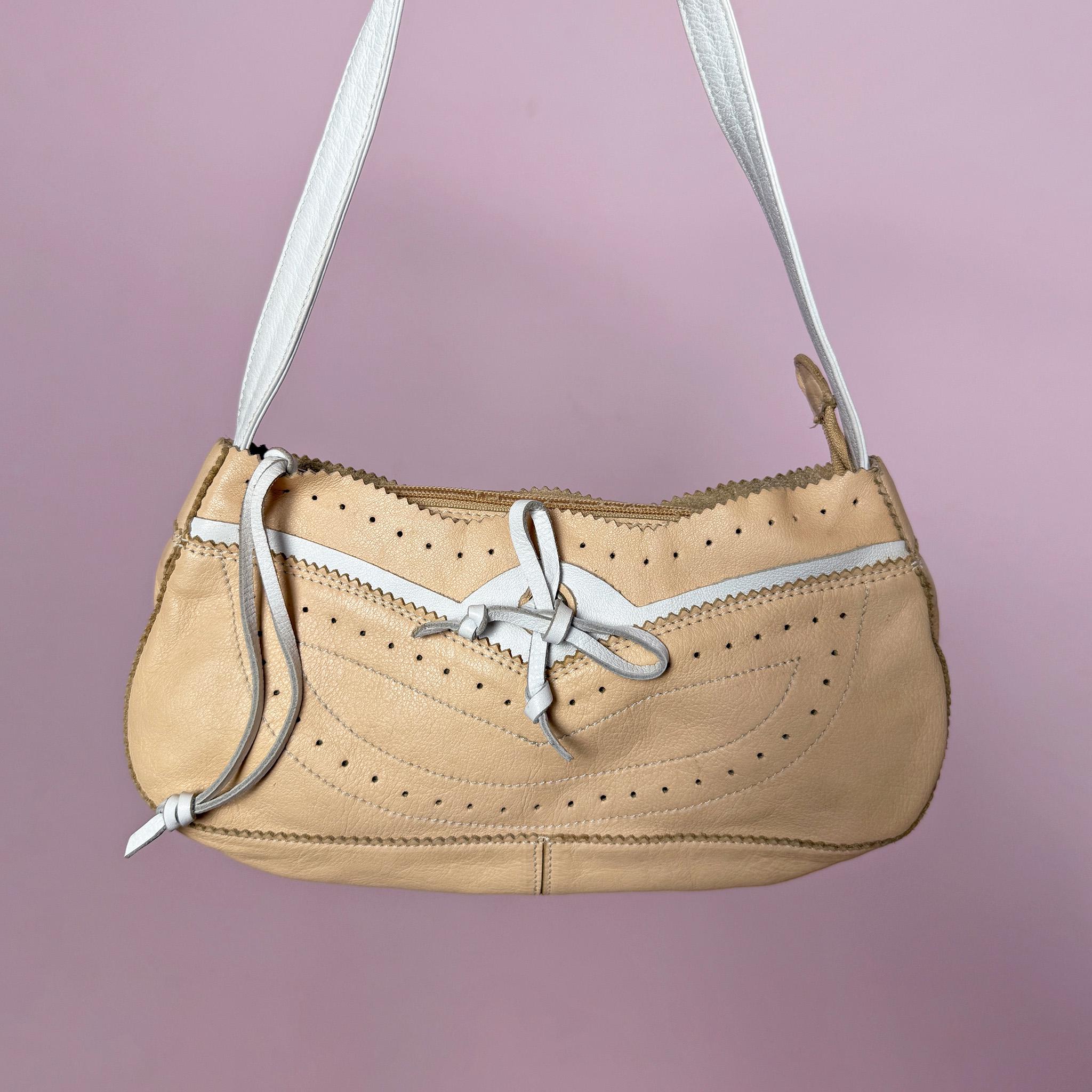 Vintage 2000s shoulder bag, made in Italy from genuine leather in a soft pastel beige and white colorway. Designed in a light baguette-style silhouette, it features a zip-top closure, a white shoulder strap, perforated detailing, contrast stitching, scalloped trim edges, and a small leather tie detail at the front. A delicate and light Y2K piece with a romantic summer feel. From an Italian brand. Excellent vintage condition.