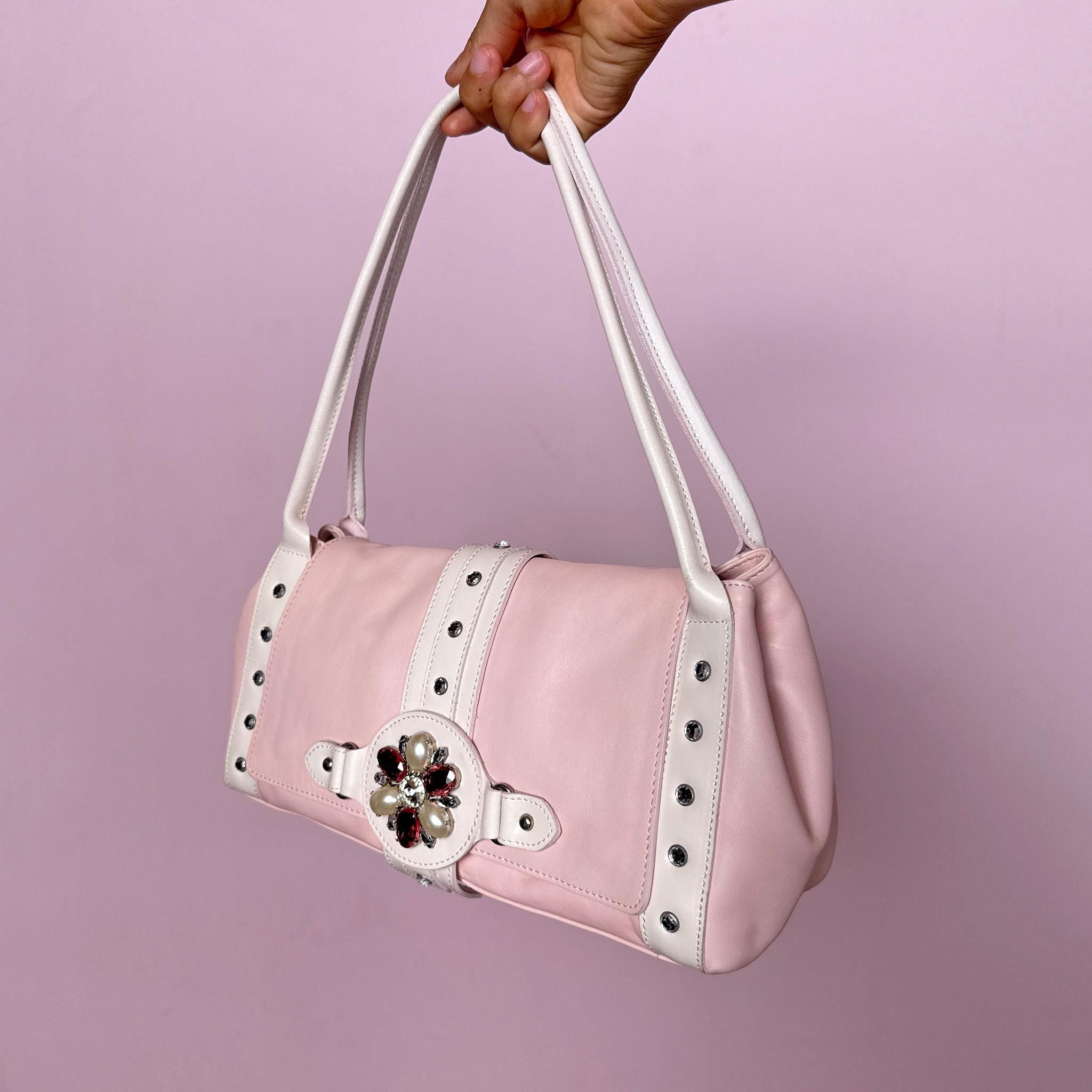 Vintage 2000s shoulder bag, made in Italy from genuine leather in a soft pastel pink and white colorway. Designed in a feminine baguette-inspired silhouette, it features a flap front with magnetic snap button closure, white leather shoulder straps, silver-tone stud details, rhinestone accents and a decorative jeweled front strap with faux pearl and pink rhinestone embellishments. A playful and eye-catching Y2K piece with a romantic rococo coquette feel.