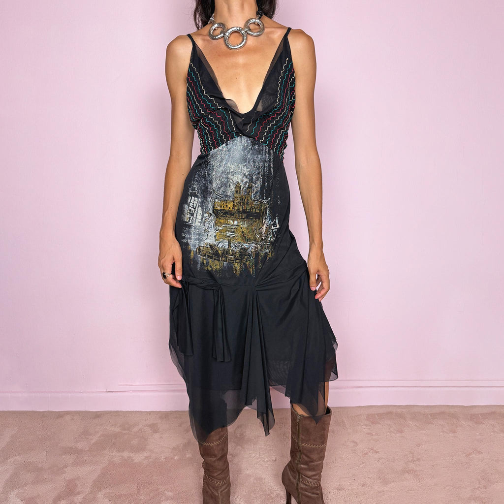 Vintage 2000s Save The Queen dress with semi-sheer mesh details and a sculptural asymmetric silhouette. Designed with thin straps, a deep V neckline, a fitted embroidered bodice with colorful zigzag stitching and a striking architectural graphic print across the front, falling into a layered black skirt with uneven sheer mesh panels and soft draped movement. A rare Italian Y2K statement piece with a dark romantic art-to-wear feel, balancing gothic fairycore