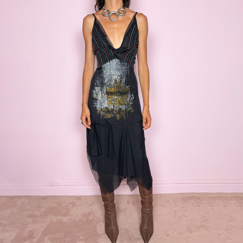 Vintage 2000s Save The Queen dress with semi-sheer mesh details and a sculptural asymmetric silhouette. Designed with thin straps, a deep V neckline, a fitted embroidered bodice with colorful zigzag stitching and a striking architectural graphic print across the front, falling into a layered black skirt with uneven sheer mesh panels and soft draped movement. A rare Italian Y2K statement piece with a dark romantic art-to-wear feel, balancing gothic fairycore
