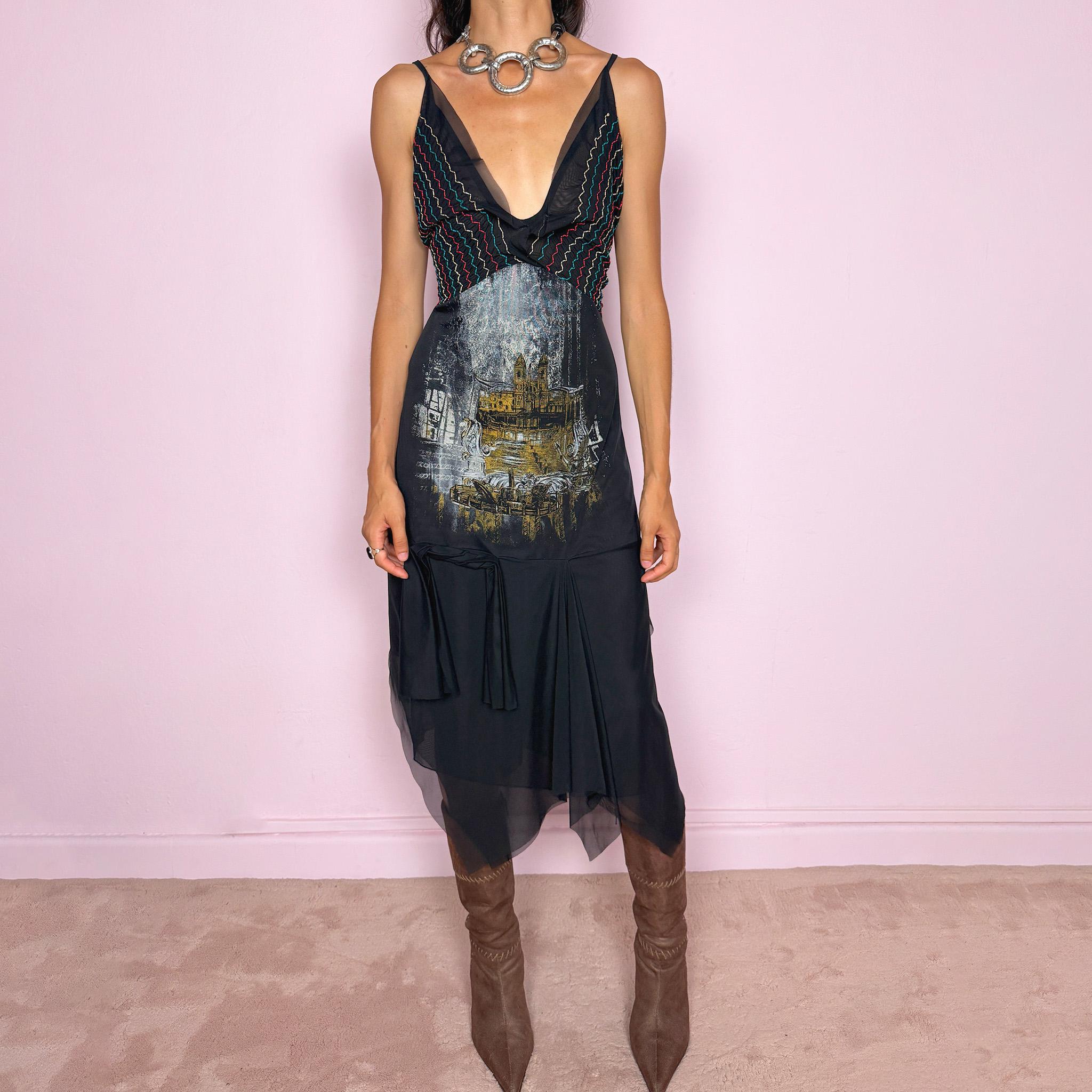Vintage 2000s Save The Queen dress with semi-sheer mesh details and a sculptural asymmetric silhouette. Designed with thin straps, a deep V neckline, a fitted embroidered bodice with colorful zigzag stitching and a striking architectural graphic print across the front, falling into a layered black skirt with uneven sheer mesh panels and soft draped movement. A rare Italian Y2K statement piece with a dark romantic art-to-wear feel, balancing gothic fairycore