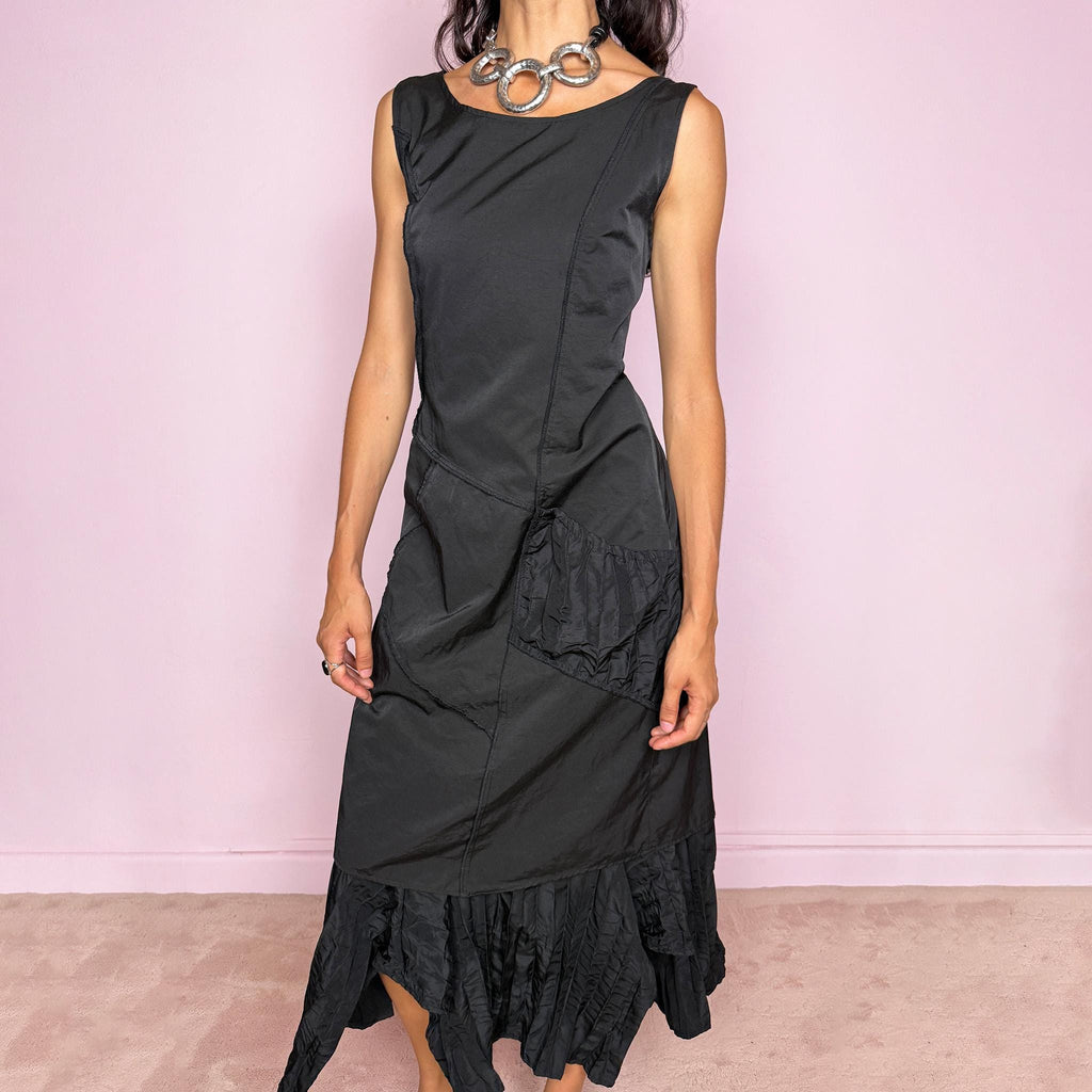 Vintage 2000s black midi dress designed in a structured no-stretch fabric with a side zip closure and an asymmetric panelled silhouette. It features a sleeveless scoop neckline, fitted upper body, diagonal seam construction, and an irregular ruffled hem with crinkled texture for sculptural movement. A dark romantic piece with an understated avant-garde feel, perfect for a minimal gothic look. Made by a French brand from 55% polyamide and 45% cotton, with a 100% polyester lining.