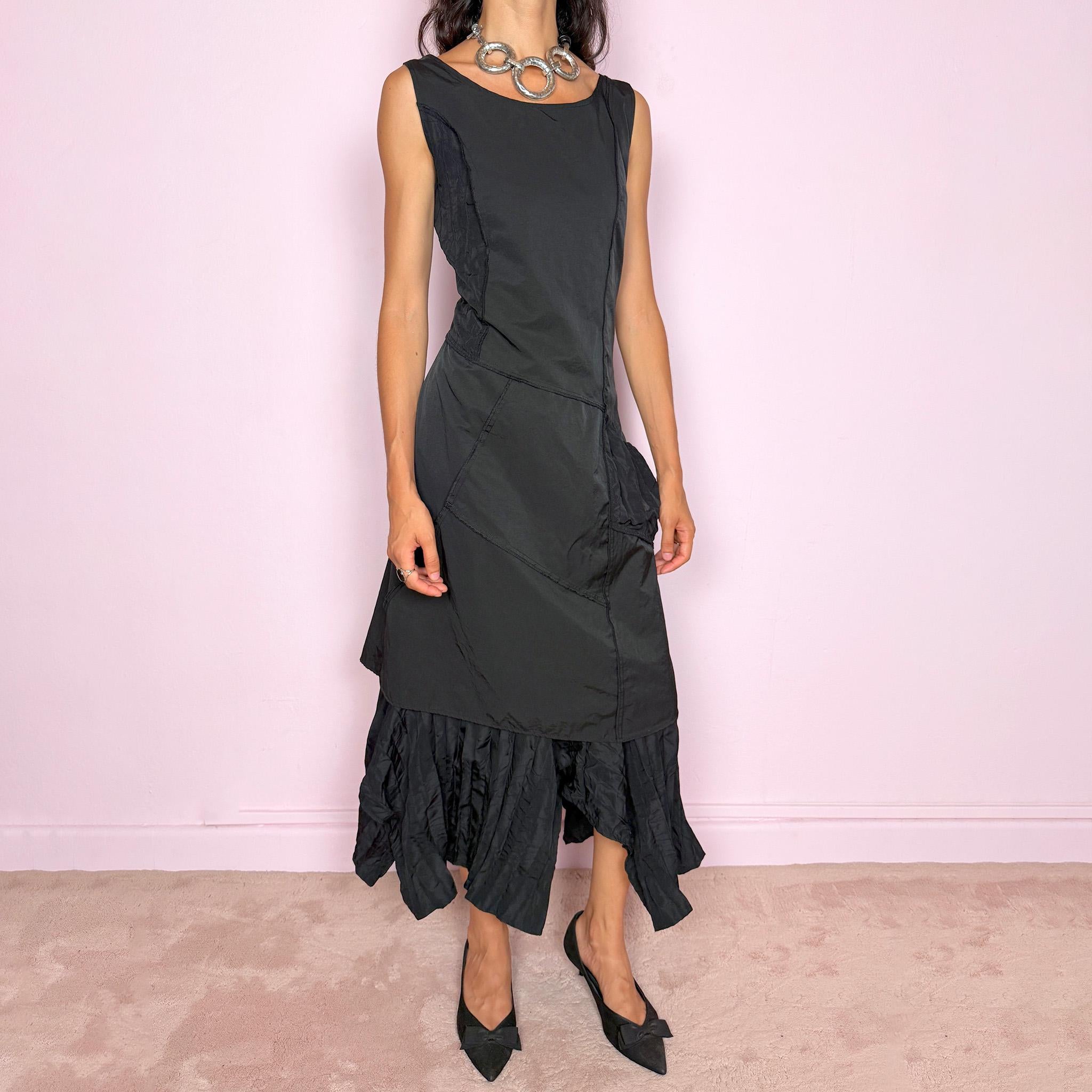 Vintage 2000s black midi dress designed in a structured no-stretch fabric with a side zip closure and an asymmetric panelled silhouette. It features a sleeveless scoop neckline, fitted upper body, diagonal seam construction, and an irregular ruffled hem with crinkled texture for sculptural movement. A dark romantic piece with an understated avant-garde feel, perfect for a minimal gothic look. Made by a French brand from 55% polyamide and 45% cotton, with a 100% polyester lining.