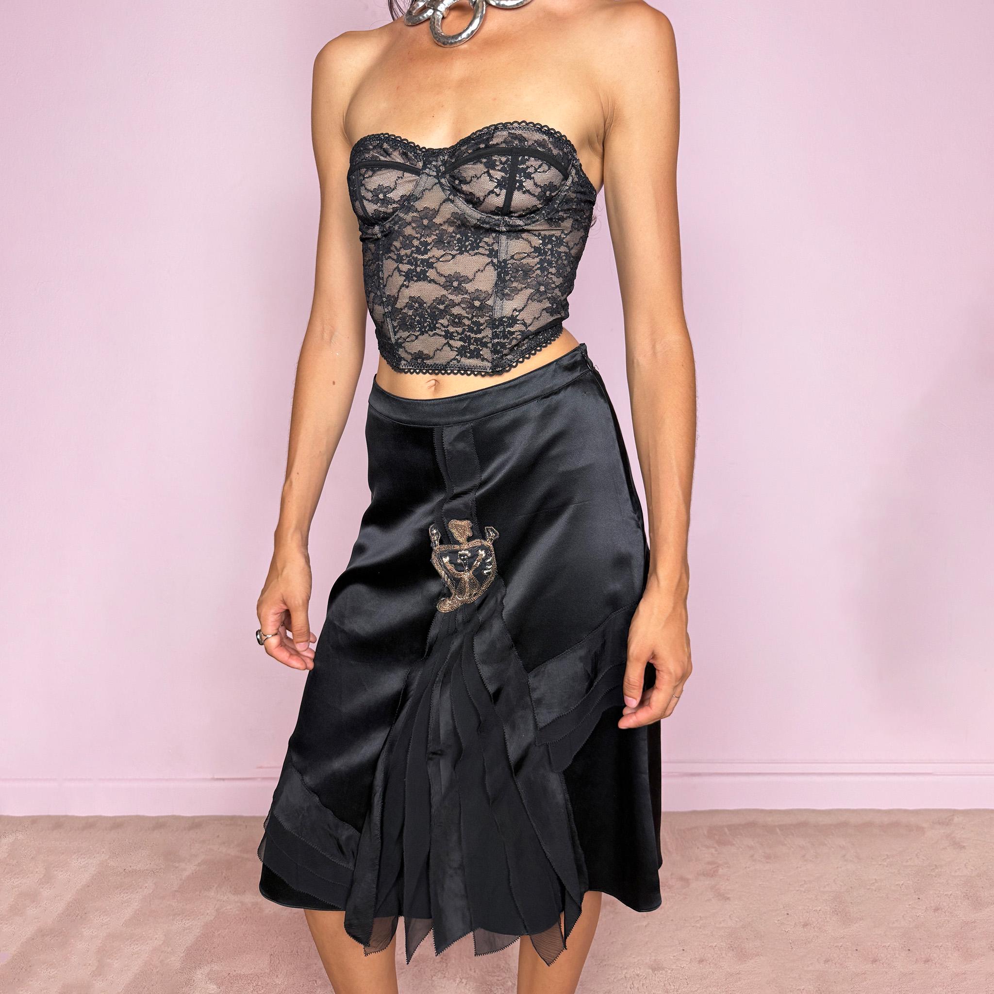 Vintage 2000s Kenzo black midi skirt crafted from 100% silk in a deep black satin finish, designed with a side zip closure and a structured no-stretch fit. It features a dramatic front detail with layered sheer pleated silk panels and an embroidered appliqué motif. A refined designer piece with a dark romantic evening feel, balancing minimal black silk with ornate Kenzo detailing. Can be worn high-waisted for size S, or slightly lower on the waist for XS and XXS. Excellent vintage condition.