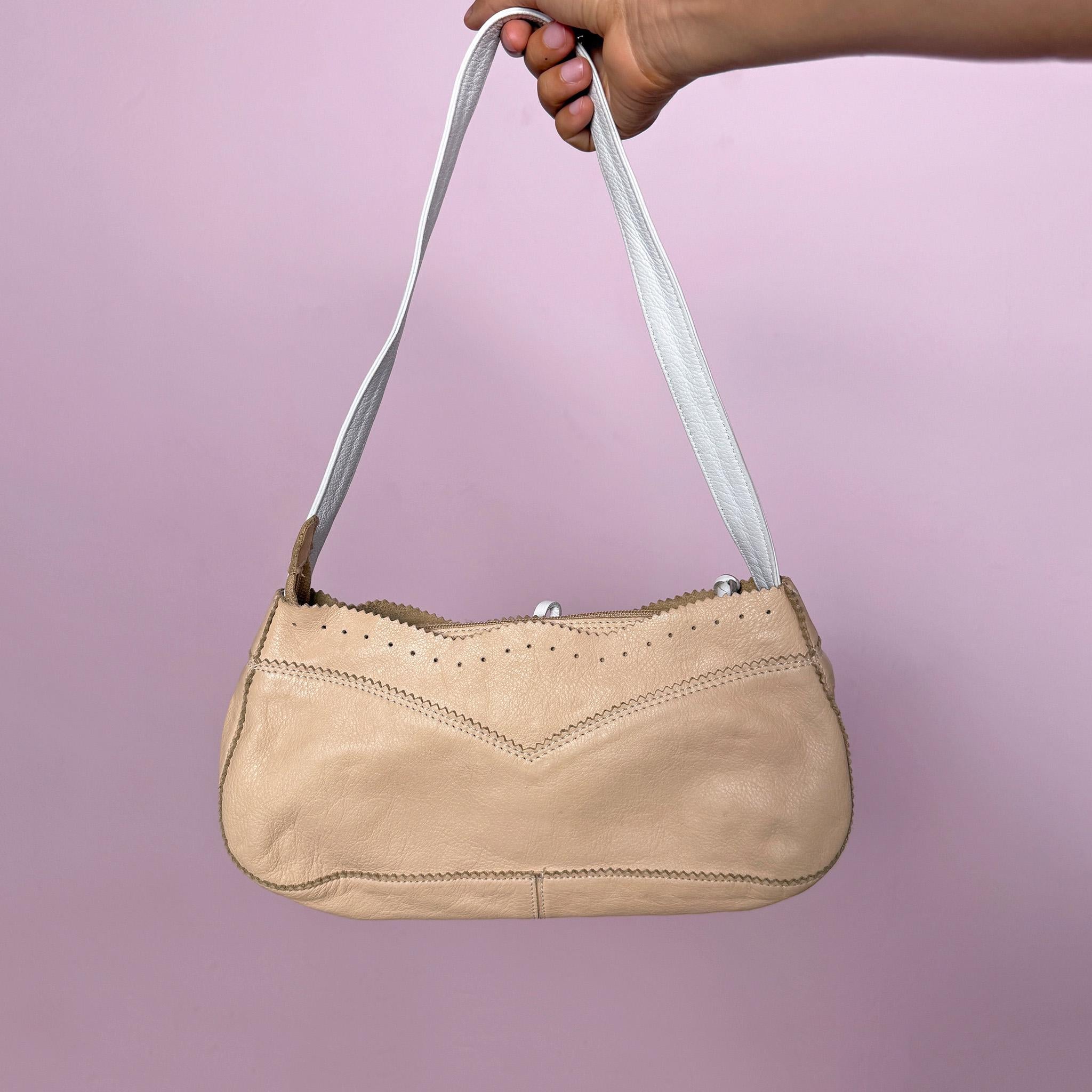 Vintage 2000s shoulder bag, made in Italy from genuine leather in a soft pastel beige and white colorway. Designed in a light baguette-style silhouette, it features a zip-top closure, a white shoulder strap, perforated detailing, contrast stitching, scalloped trim edges, and a small leather tie detail at the front. A delicate and light Y2K piece with a romantic summer feel. From an Italian brand. Excellent vintage condition.