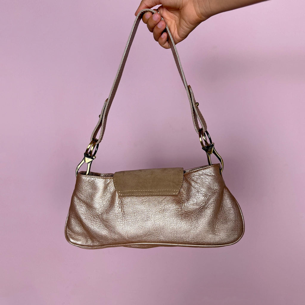Vintage 2000s shoulder bag made in Italy in a beautiful metallic bronze-taupe shade with warm golden undertones. Designed with a baguette silhouette, statement buckle-inspired front detailing with antique brass-tone hardware, a shoulder strap, and a suede front flap. Finished with a zip-top closure. The interior label states "Genuine Leather". Excellent vintage condition.
