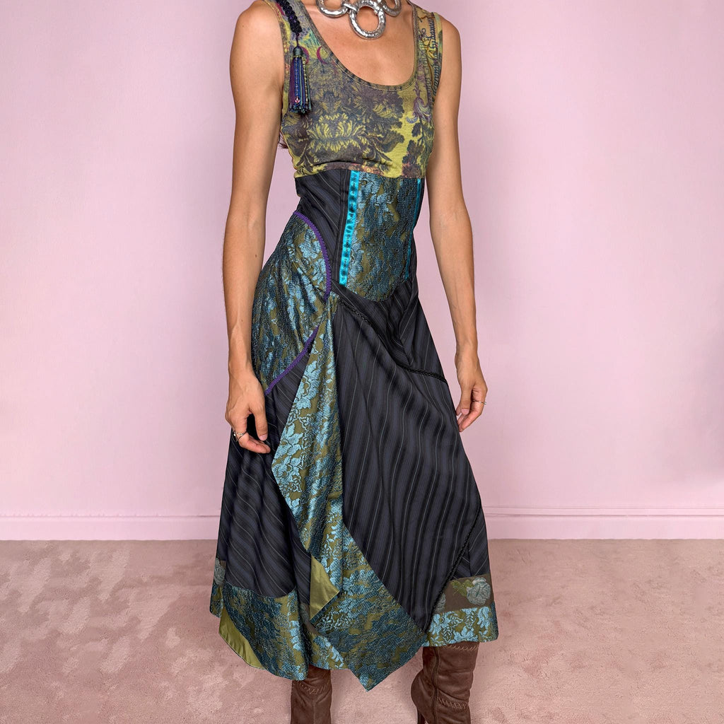 Vintage 2000s midi dress designed with a dramatic, medieval-inspired avant-garde silhouette. It features a graphic bust panel with green multicolored abstract artwork, a fitted waist with blue lace panels, a side zip closure, and a flowing asymmetric skirt with mixed striped fabrics, contrast trims, and layered draped sections that create sculptural movement. A rare fantasy statement piece with a theatrical baroque feel.