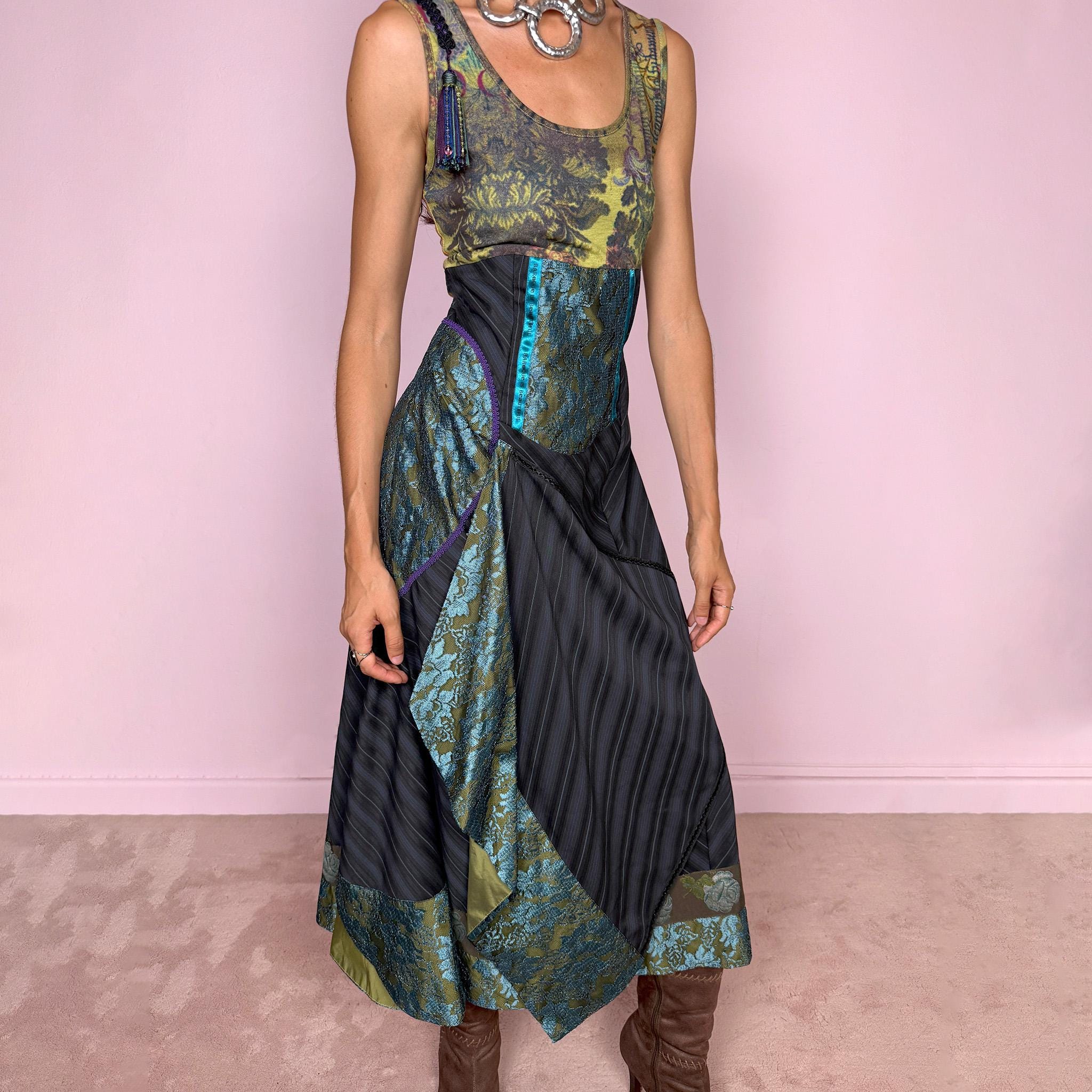 Vintage 2000s midi dress designed with a dramatic, medieval-inspired avant-garde silhouette. It features a graphic bust panel with green multicolored abstract artwork, a fitted waist with blue lace panels, a side zip closure, and a flowing asymmetric skirt with mixed striped fabrics, contrast trims, and layered draped sections that create sculptural movement. A rare fantasy statement piece with a theatrical baroque feel.