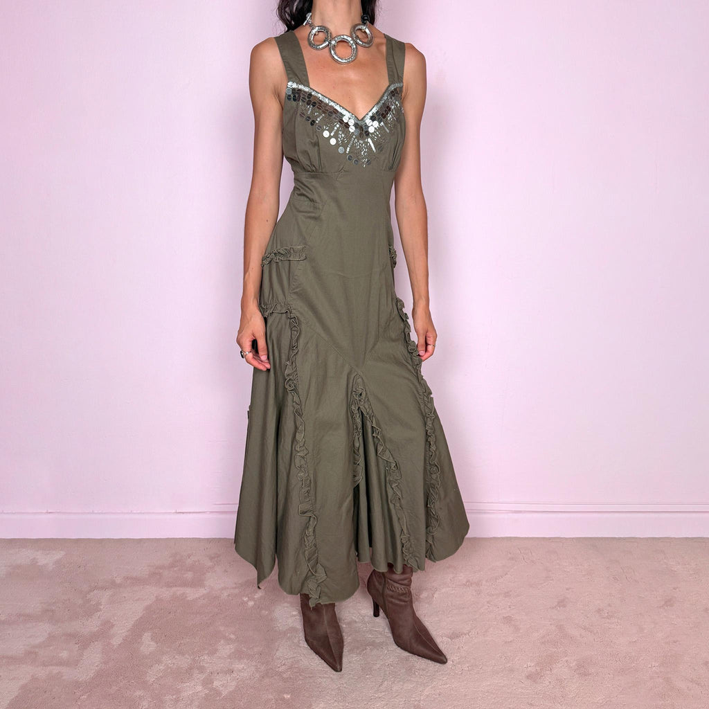 Vintage 2000s khaki green maxi dress crafted from 100% cotton, featuring a fitted empire-waist silhouette, wide shoulder straps, and a softly flared asymmetric hem. The neckline is heavily embellished with metallic silver sequins and beading arranged in a statement geometric pattern, contrasting with the earthy cotton fabric. Finished with sculptural panel construction and delicate ruffled trim running along the skirt seams.