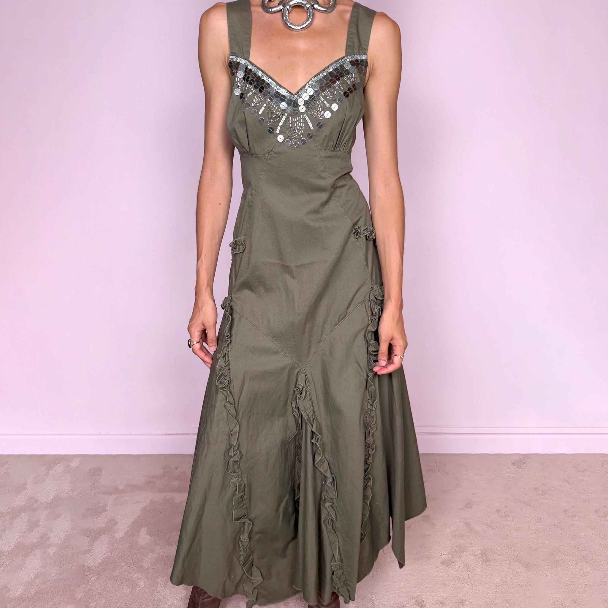 Vintage 2000s khaki green maxi dress crafted from 100% cotton, featuring a fitted empire-waist silhouette, wide shoulder straps, and a softly flared asymmetric hem. The neckline is heavily embellished with metallic silver sequins and beading arranged in a statement geometric pattern, contrasting with the earthy cotton fabric. Finished with sculptural panel construction and delicate ruffled trim running along the skirt seams.