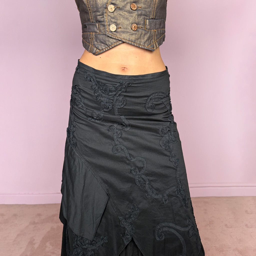 Vintage 2000s black midi skirt crafted from 100% cotton with layered asymmetric panels and tonal floral embroidery appliqué. Features a back zip closure and no stretch. Ideal for bohemian, dark fairy, or summer styling. Can be worn high-waisted for size S or slightly lower on the waist for sizes XS–XXS. Made in France by a French brand and fully lined in 100% polyester. Excellent vintage condition.