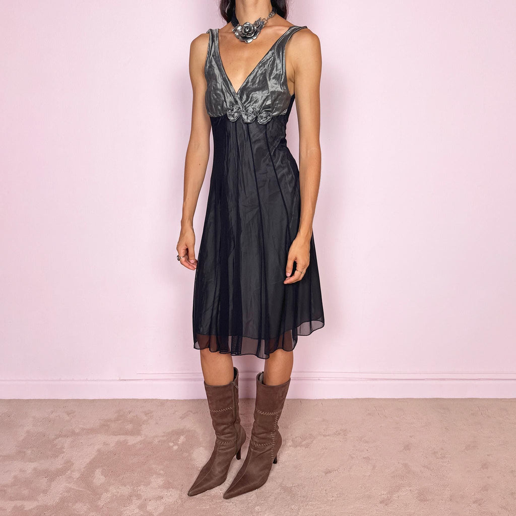 Vintage 2000s sleeveless midi dress made in Italy. Designed with a fitted empire-line silhouette, a deep V-neckline, and a contrasting metallic grey bodice with a soft gathered texture and dimensional rosette appliqués beneath the bust. The black semi-sheer skirt falls fluidly, creating an elegant dark romantic silhouette ideal for evenings and parties. Made from a non-stretch polyester, polyamide, cotton, and metal blend. Excellent vintage condition.