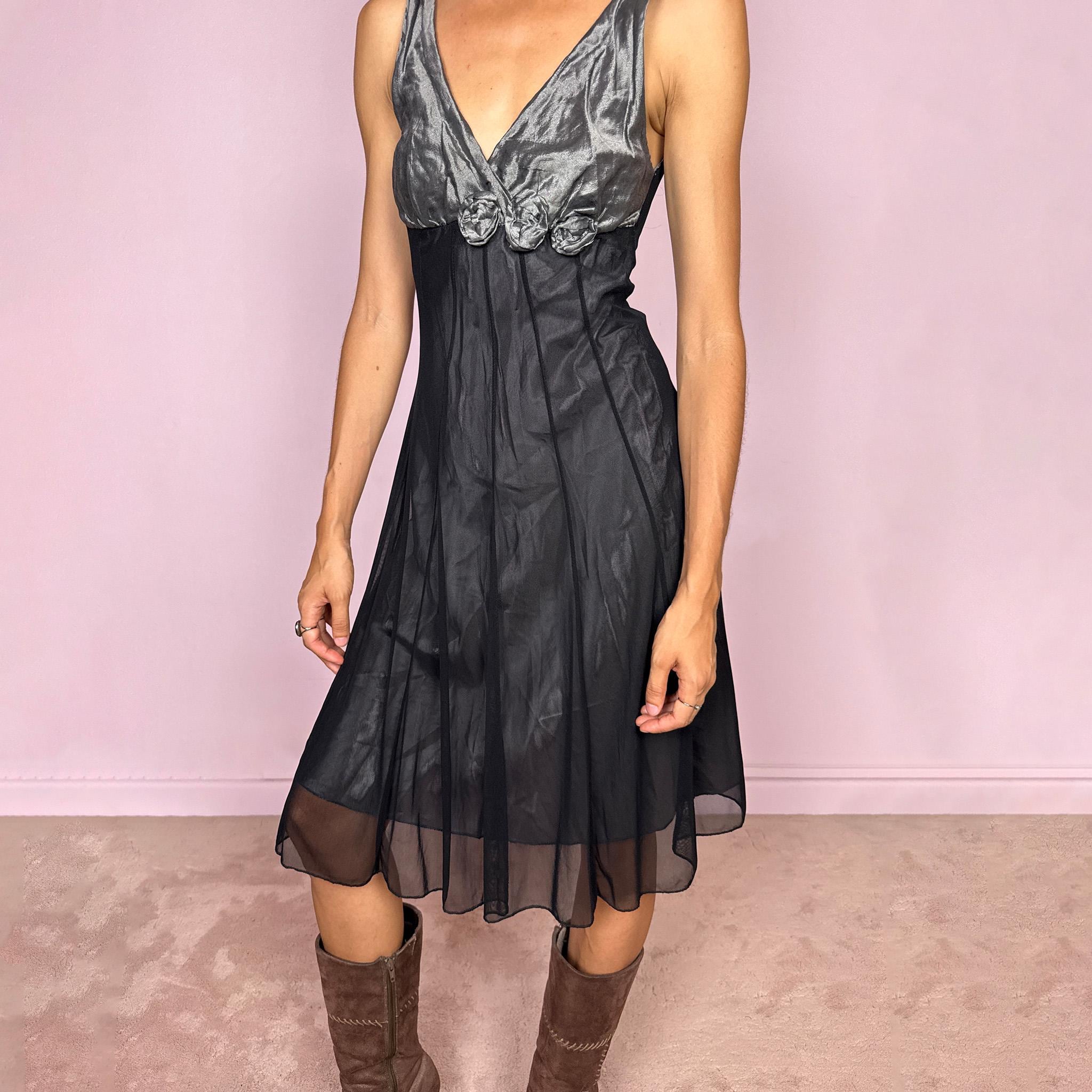 Vintage 2000s sleeveless midi dress made in Italy. Designed with a fitted empire-line silhouette, a deep V-neckline, and a contrasting metallic grey bodice with a soft gathered texture and dimensional rosette appliqués beneath the bust. The black semi-sheer skirt falls fluidly, creating an elegant dark romantic silhouette ideal for evenings and parties. Made from a non-stretch polyester, polyamide, cotton, and metal blend. Excellent vintage condition.