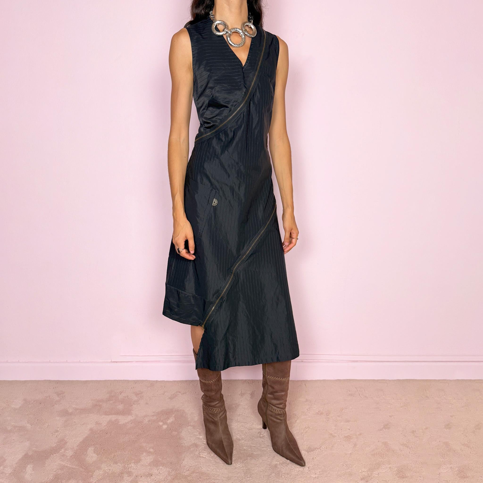 Vintage 2000s black asymmetric midi dress crafted from structured fabric with subtle tonal pinstripes, featuring a fitted sleeveless silhouette, deep V-neckline, and dramatic diagonal exposed zip detailing running across the body. Sculptural asymmetric panel construction creates a deconstructed, avant-garde silhouette with a dark utilitarian feel. Features a side zip closure and no stretch. Made in France by a French brand from 68% cotton and 32% polyamide. Excellent vintage condition.