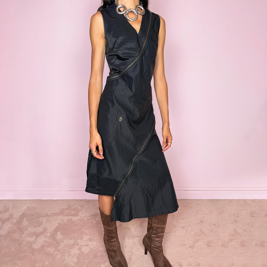 Vintage 2000s black asymmetric midi dress crafted from structured fabric with subtle tonal pinstripes, featuring a fitted sleeveless silhouette, deep V-neckline, and dramatic diagonal exposed zip detailing running across the body. Sculptural asymmetric panel construction creates a deconstructed, avant-garde silhouette with a dark utilitarian feel. Features a side zip closure and no stretch. Made in France by a French brand from 68% cotton and 32% polyamide. Excellent vintage condition.