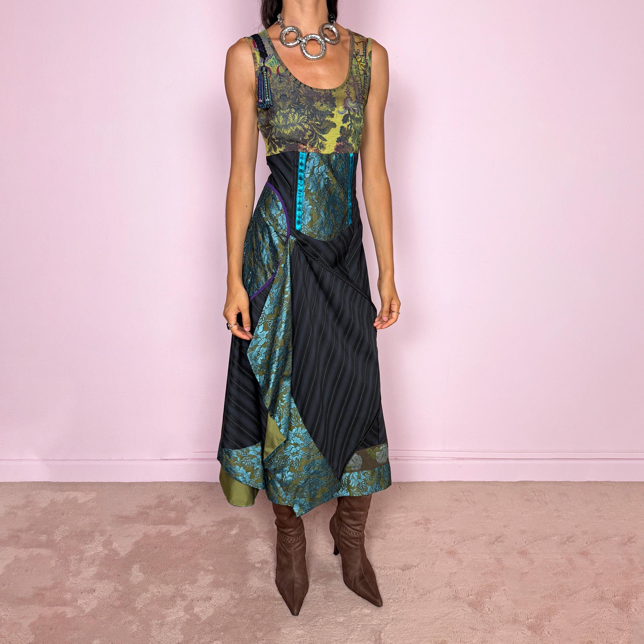 Vintage 2000s midi dress designed with a dramatic, medieval-inspired avant-garde silhouette. It features a graphic bust panel with green multicolored abstract artwork, a fitted waist with blue lace panels, a side zip closure, and a flowing asymmetric skirt with mixed striped fabrics, contrast trims, and layered draped sections that create sculptural movement. A rare fantasy statement piece with a theatrical baroque feel.