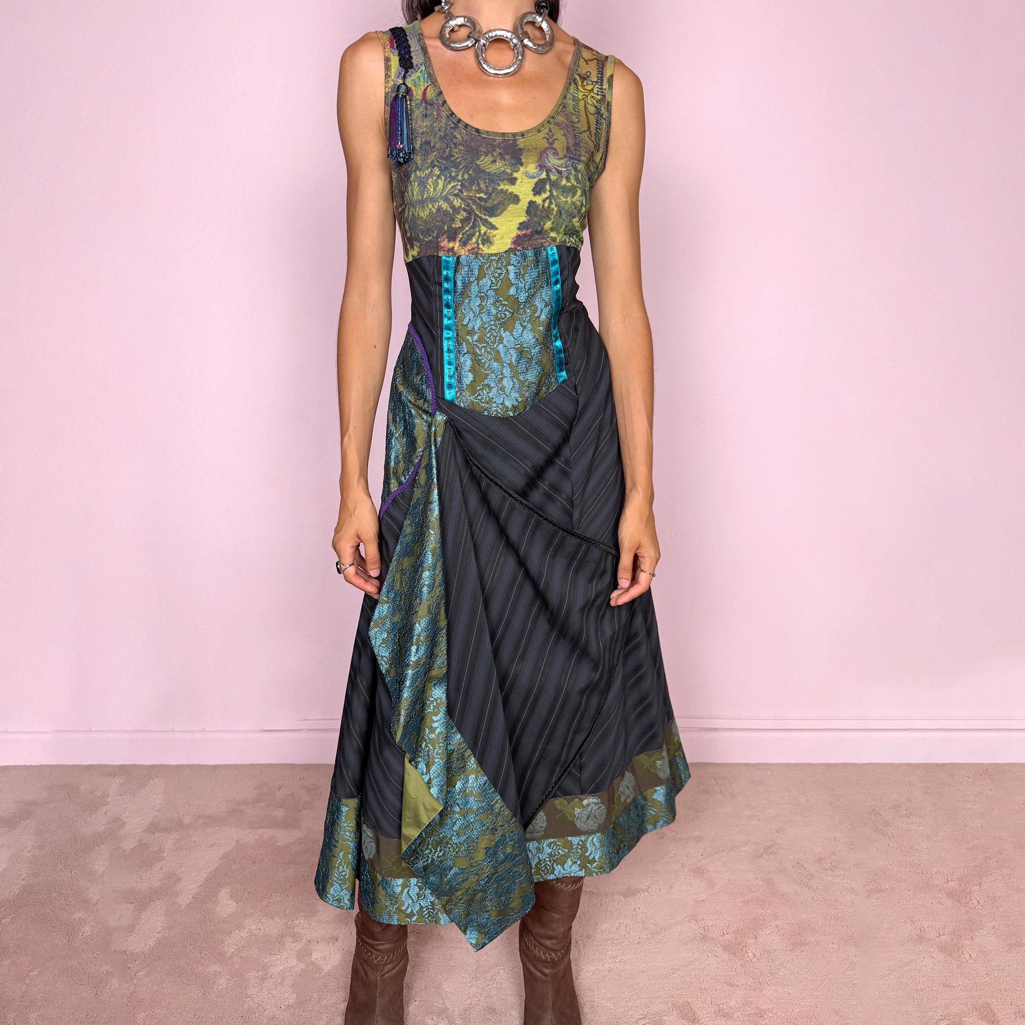 Vintage 2000s midi dress designed with a dramatic, medieval-inspired avant-garde silhouette. It features a graphic bust panel with green multicolored abstract artwork, a fitted waist with blue lace panels, a side zip closure, and a flowing asymmetric skirt with mixed striped fabrics, contrast trims, and layered draped sections that create sculptural movement. A rare fantasy statement piece with a theatrical baroque feel.