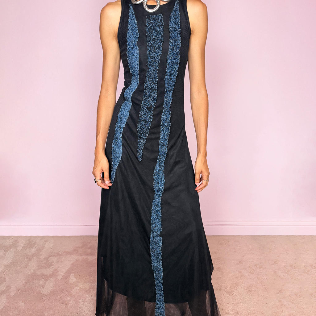 Vintage 2000s maxi dress crafted from stretchy black mesh with a fitted sleeveless silhouette, a semi-sheer outer layer, and an asymmetric flowing hem. Detailed with contrasting blue embroidered threadwork running vertically across the body, creating a textured effect with a distinctly avant-garde Y2K feel. Made in Italy by an Italian brand from 100% polyamide. Excellent vintage condition.