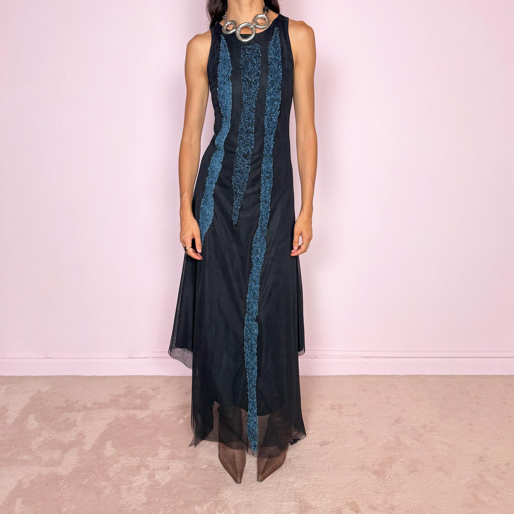 Vintage 2000s maxi dress crafted from stretchy black mesh with a fitted sleeveless silhouette, a semi-sheer outer layer, and an asymmetric flowing hem. Detailed with contrasting blue embroidered threadwork running vertically across the body, creating a textured effect with a distinctly avant-garde Y2K feel. Made in Italy by an Italian brand from 100% polyamide. Excellent vintage condition.