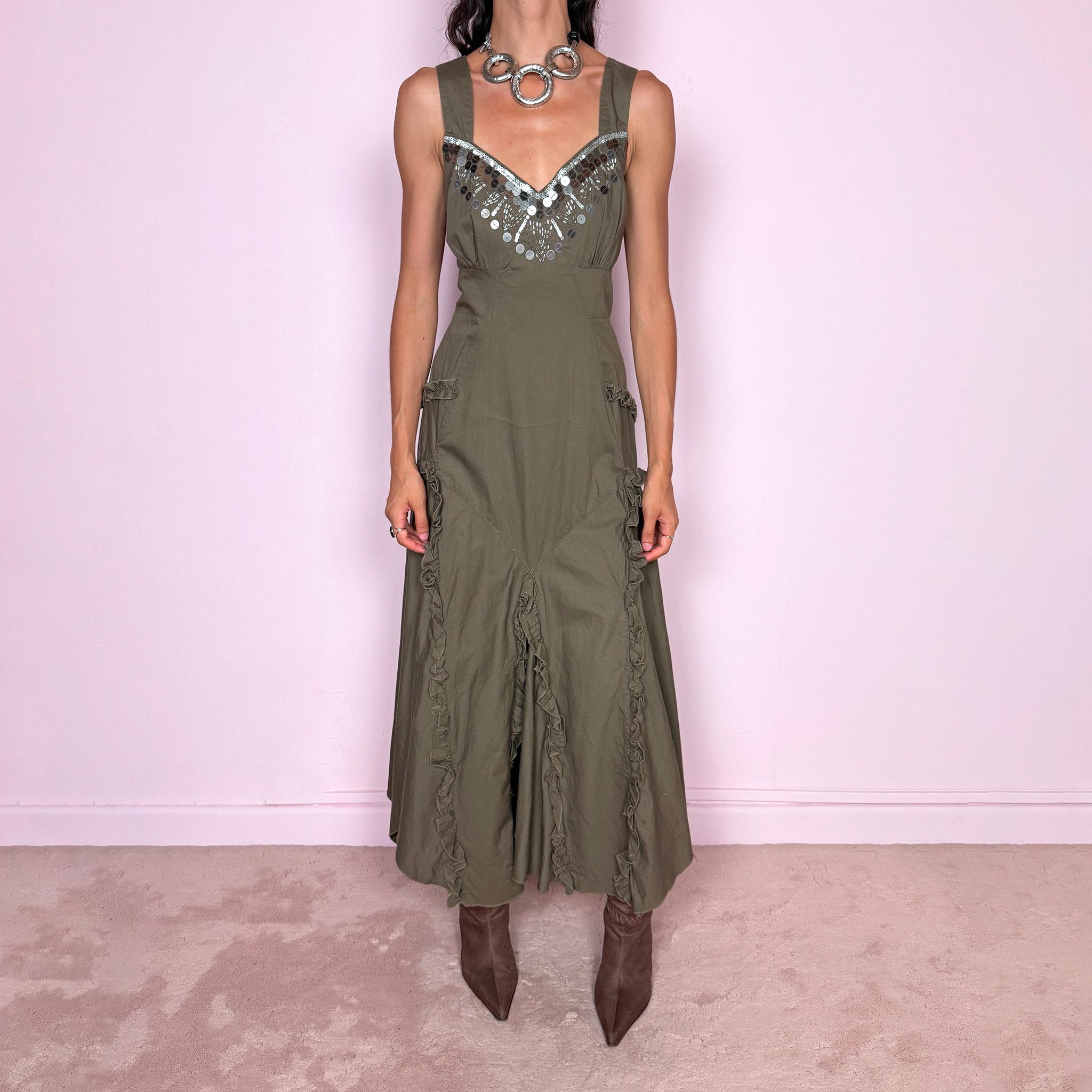 Vintage 2000s khaki green maxi dress crafted from 100% cotton, featuring a fitted empire-waist silhouette, wide shoulder straps, and a softly flared asymmetric hem. The neckline is heavily embellished with metallic silver sequins and beading arranged in a statement geometric pattern, contrasting with the earthy cotton fabric. Finished with sculptural panel construction and delicate ruffled trim running along the skirt seams.