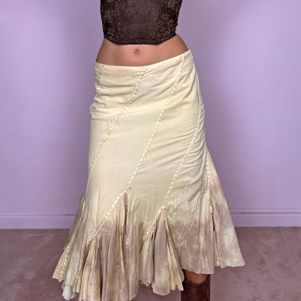 Vintage 2000s light yellow asymmetric midi skirt with a romantic, deconstructed silhouette, featuring curved diagonal paneling, visible contrast stitching, and flared godet inserts. Finished with a tie-dye effect concentrated around the lower panels and raw hem. Non-stretch fabric with a side zip closure. Can be worn mid-rise for size S or lower-rise for size XS. Ideal for bohemian, fairy-inspired, earthy, rustic, and organic summer styling.