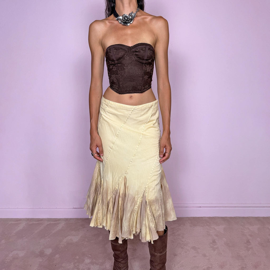Vintage 2000s light yellow asymmetric midi skirt with a romantic, deconstructed silhouette, featuring curved diagonal paneling, visible contrast stitching, and flared godet inserts. Finished with a tie-dye effect concentrated around the lower panels and raw hem. Non-stretch fabric with a side zip closure. Can be worn mid-rise for size S or lower-rise for size XS. Ideal for bohemian, fairy-inspired, earthy, rustic, and organic summer styling.