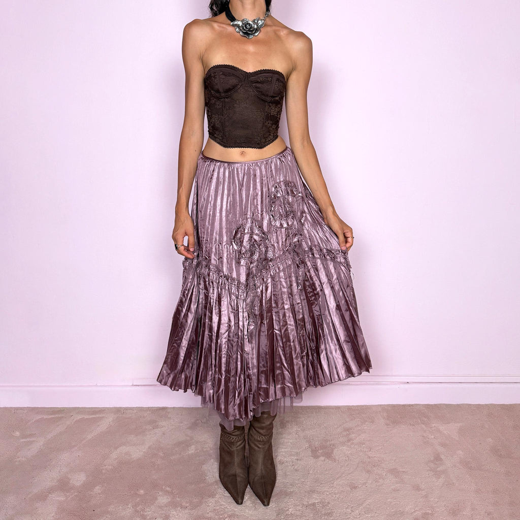 Vintage 2000s dusty mauve metallic midi skirt featuring intricate all-over pleating with a fluid iridescent sheen, sculptural floral appliqué details, and sheer tulle fabric peeking from underneath the hem. Ideal for parties or dreamy, romantic elevated outfits. Can be worn high-waisted for size S or lower on the waist for size XS. From a French brand. Crafted from 100% polyester with no stretch and finished with a side zip closure. Excellent vintage condition.
