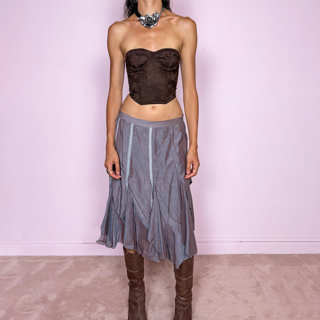Vintage 2000s bluish-gray iridescent midi skirt featuring a subtle sheen that shifts between dusty blue, gray, and muted mauve tones. Designed with a fluid asymmetric layered construction, curved paneling, delicate lace-trim inserts, and an irregular hem that creates soft movement and a deconstructed silhouette. Perfect for delicate, ethereal styling. Features a back zip closure and no stretch. Can be worn high-waisted for size M or lower-rise for sizes XS–S. Made from 70% cotton and 30% silk