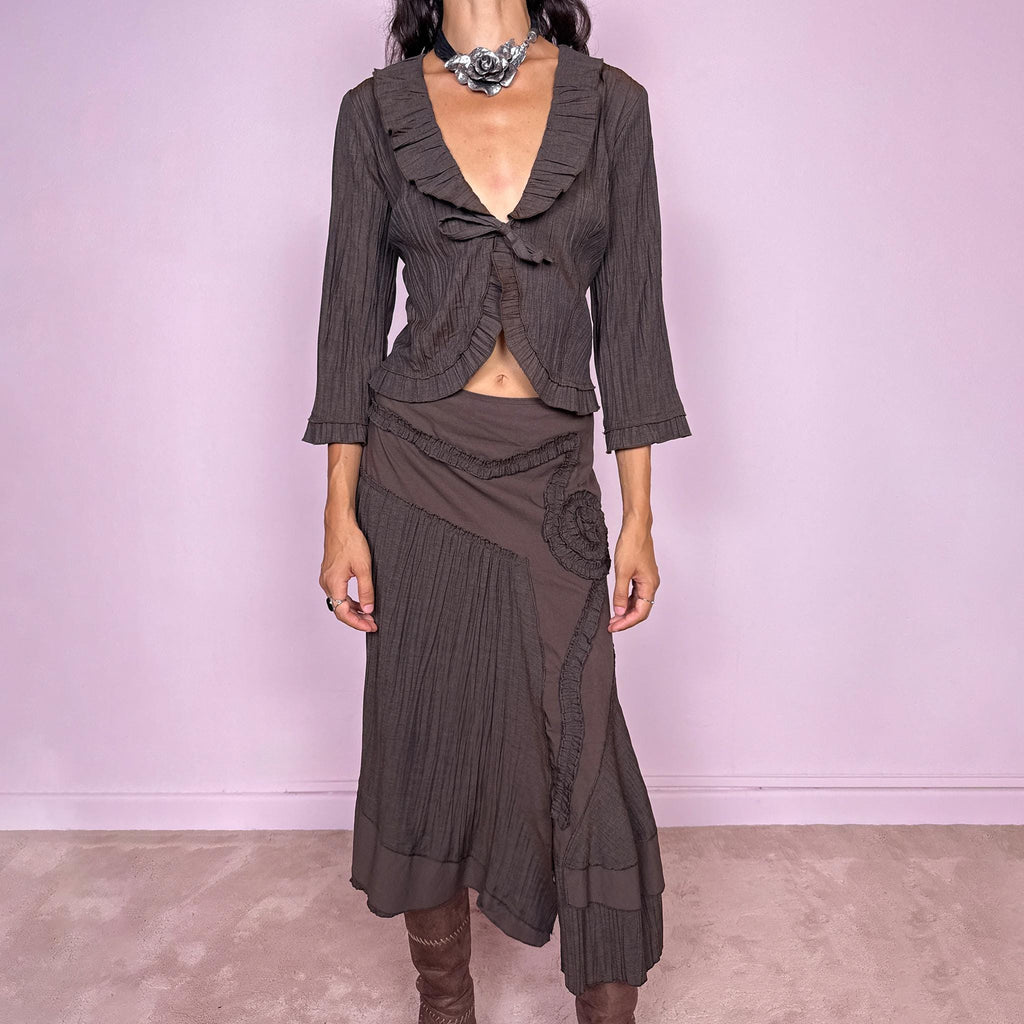 Vintage 2000s brown two-piece set featuring a fitted tie-front top with softly flared 3/4 sleeves and delicate ruffle trim, paired with a matching asymmetric midi skirt. The skirt combines fluid paneling, pleated inserts, ruffled appliqué detailing, and an irregular hem for a romantic deconstructed Y2K silhouette, with a side zip closure. Can be worn high-waisted for size S or slightly lower on the waist for size XS. Made from a non-stretch polyester and viscose blend.