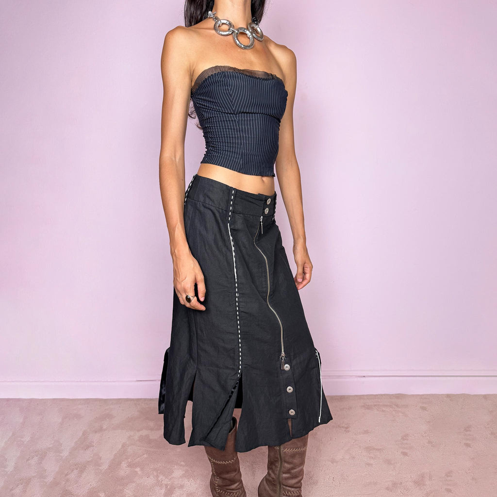 Vintage 2000s black midi skirt featuring an exposed full-length front zip, double-button waistband, and contrast white stitching throughout. The lower section opens into sculptural deconstructed panels with additional button and zip detailing, creating an asymmetric, utilitarian avant-garde feel. Can be worn high-waisted for size M or slightly lower on the waist for sizes S and XS. Non-stretch. Made in Holland by a Dutch brand from a structured blend of 52% cotton and 48% linen