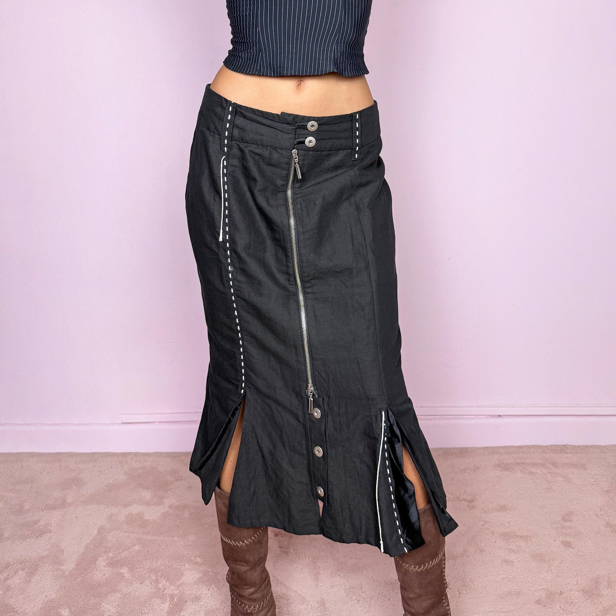Vintage 2000s black midi skirt featuring an exposed full-length front zip, double-button waistband, and contrast white stitching throughout. The lower section opens into sculptural deconstructed panels with additional button and zip detailing, creating an asymmetric, utilitarian avant-garde feel. Can be worn high-waisted for size M or slightly lower on the waist for sizes S and XS. Non-stretch. Made in Holland by a Dutch brand from a structured blend of 52% cotton and 48% linen
